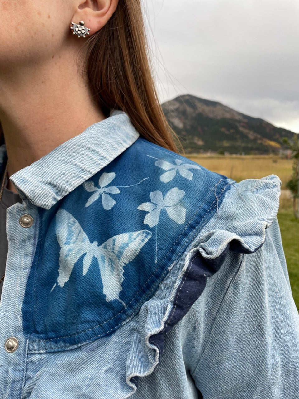 Close-up of jean jacket with cyanotype butterfly and flower design, mountains in the background.