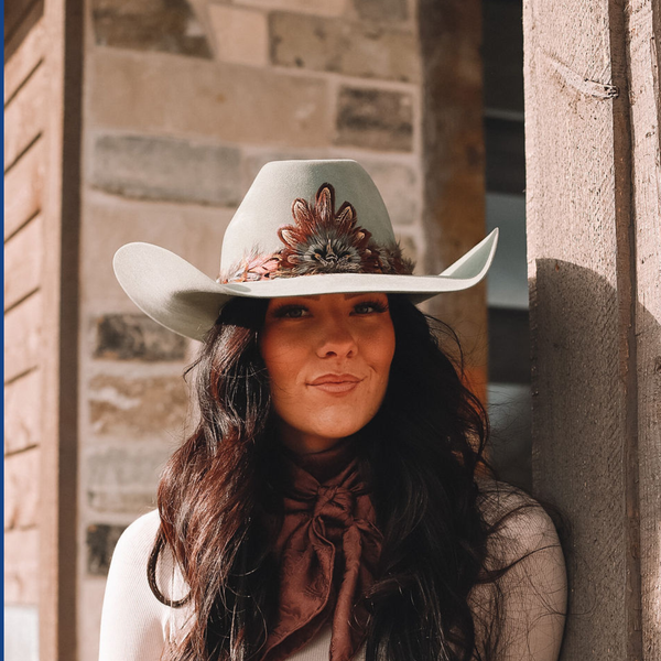 Woman wearing a cowboy hat with a beautifully ornate feather medallion and hatband displayed. 