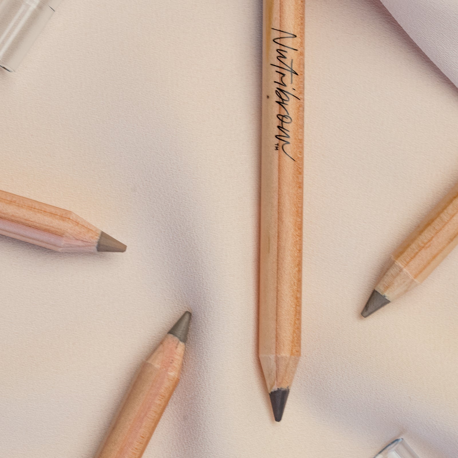 Flat lay of several Crunchi Nutribrow pencils scattered on a neutral background, showing clean packaging design.