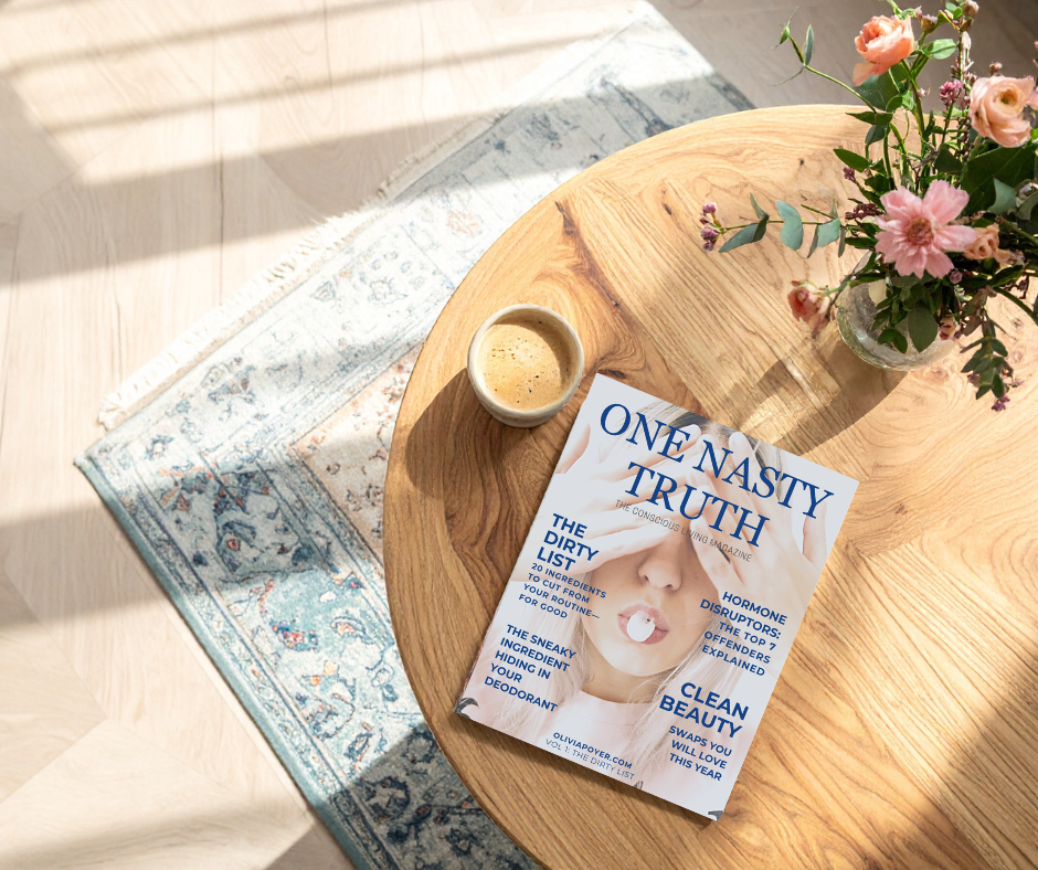 Flat lay of the “One Nasty Truth” magazine on a wooden table beside a mug of coffee, with a blue patterned rug partially visible in the background.