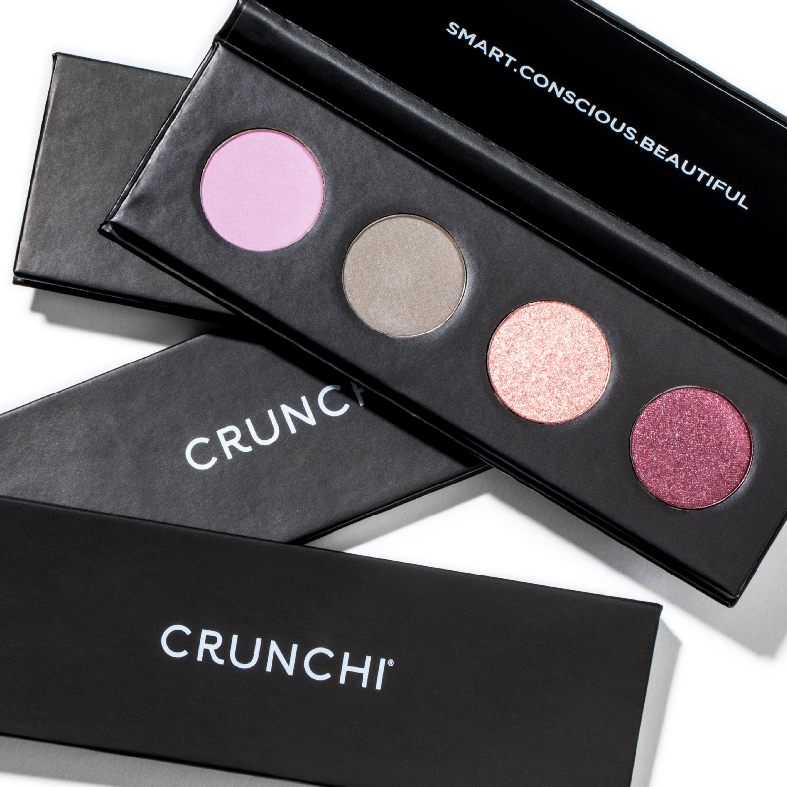 Stack of Crunchi Shadow Bar eyeshadow palettes showing four complementary shades per palette, neutral background.