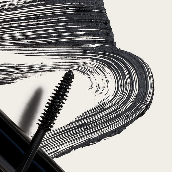 Crunchi Shattered Mascara wand and black pigment swiped across white background, showing buildable texture.