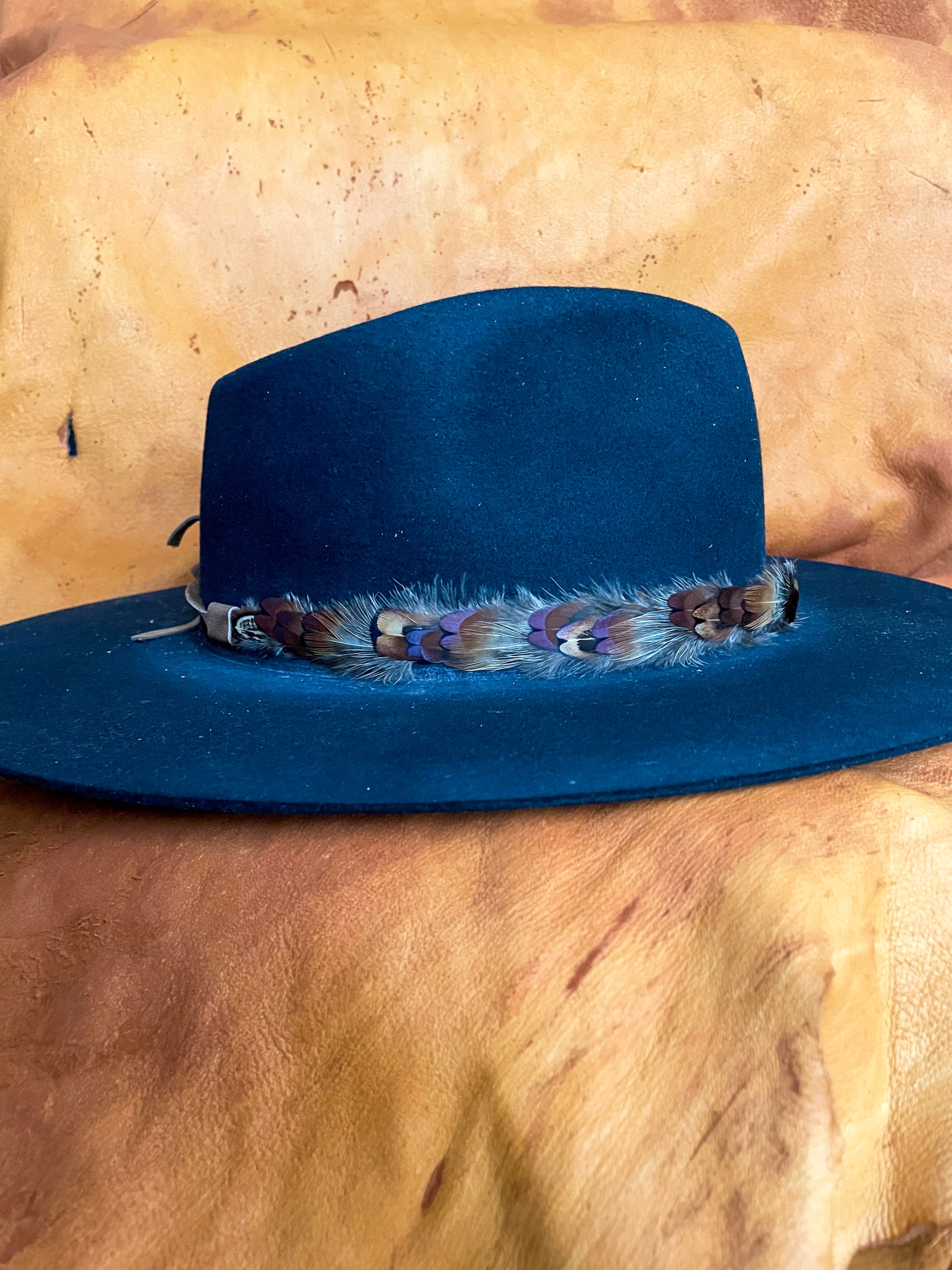 A side view of a handmade feather hatband with rust, blue, and golden pheasant feathers on a black felt hat.