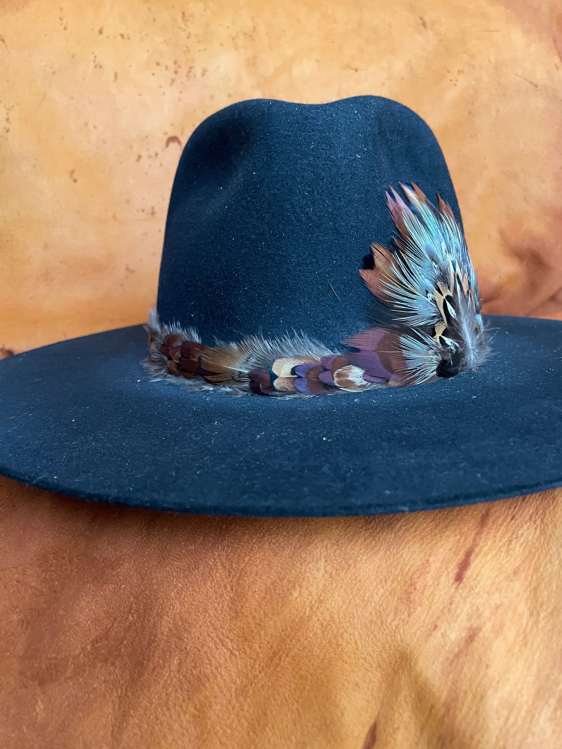 The front view of a black felt hat with a one of a kind hatband and matching medallion. 