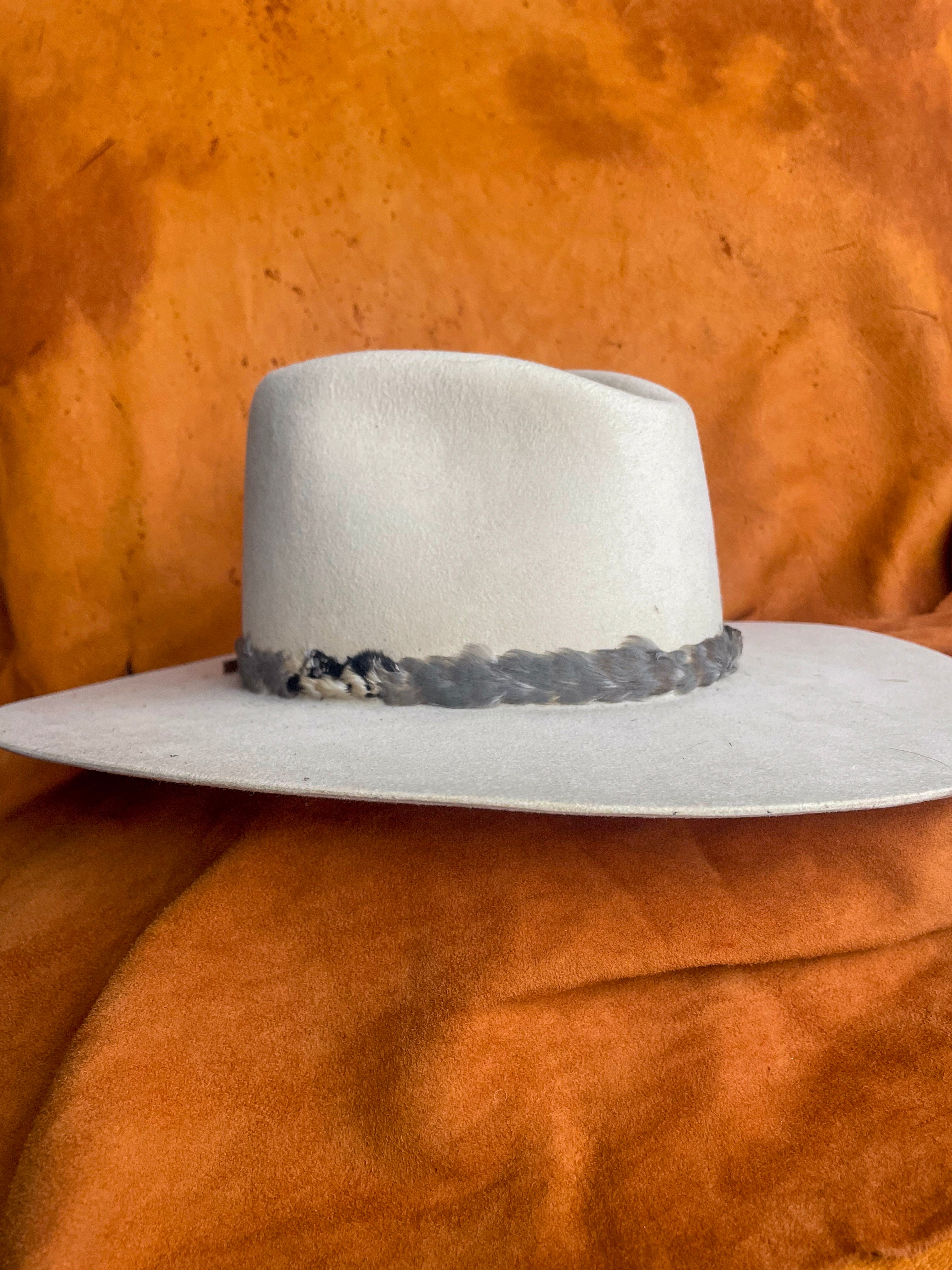 Close-up of soft blue-grey and neutral colored feather hatband on a creamy white felt hat. 