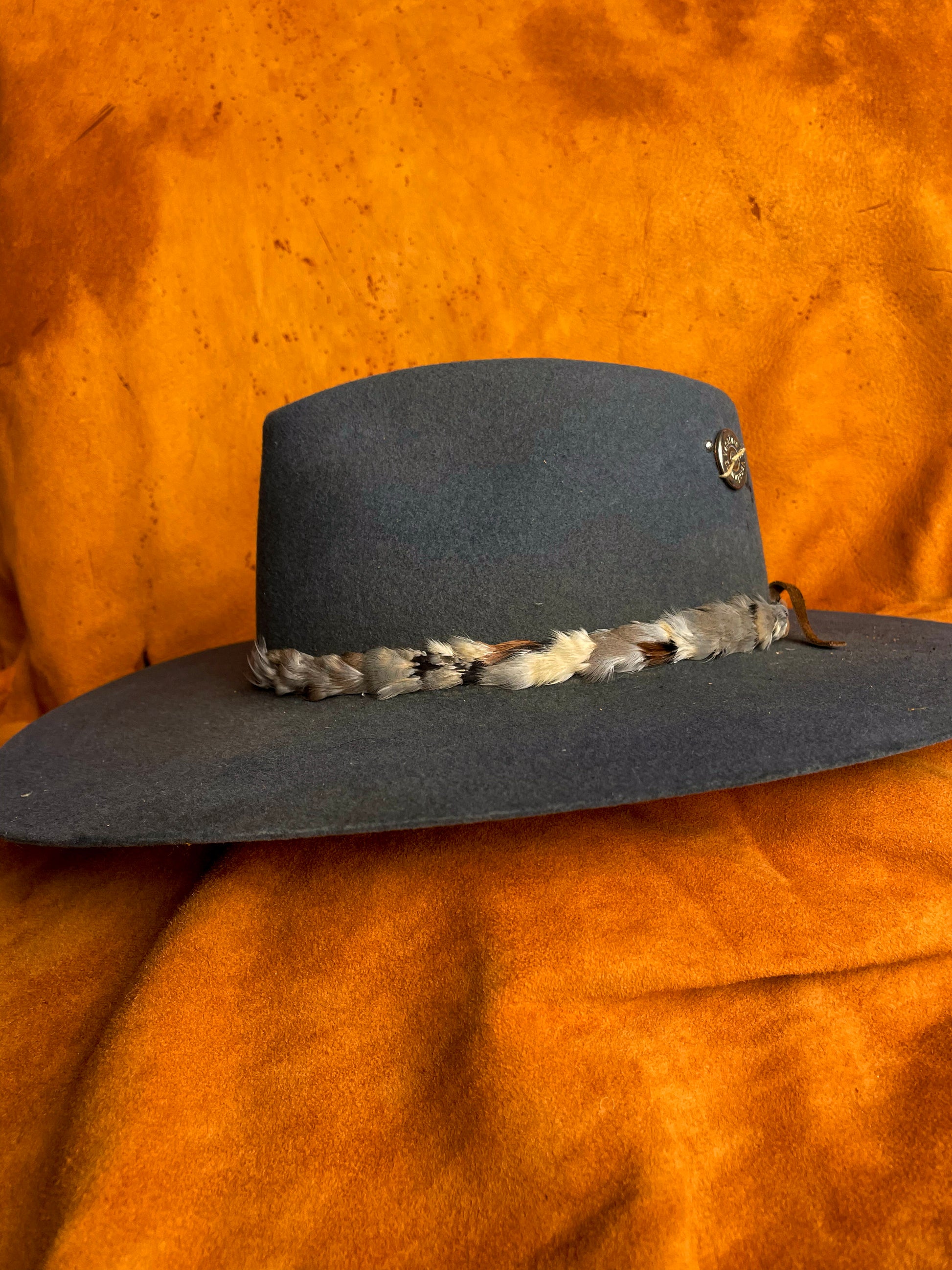 Side view of a handmade chukar feather hatband with blue, grey, and cream tones on a steel blue felt hat. 