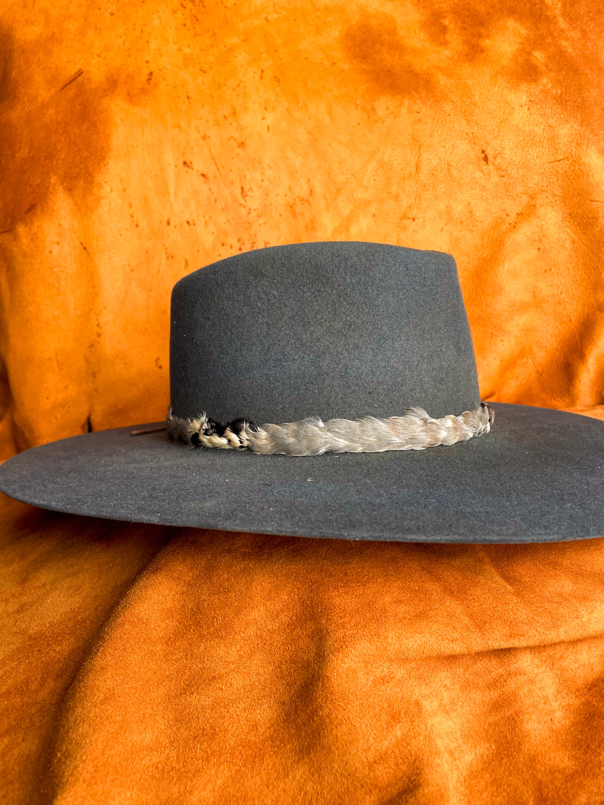 Front angle view of a cool toned chukar feather hat band styled on a steel blue felt hat. 