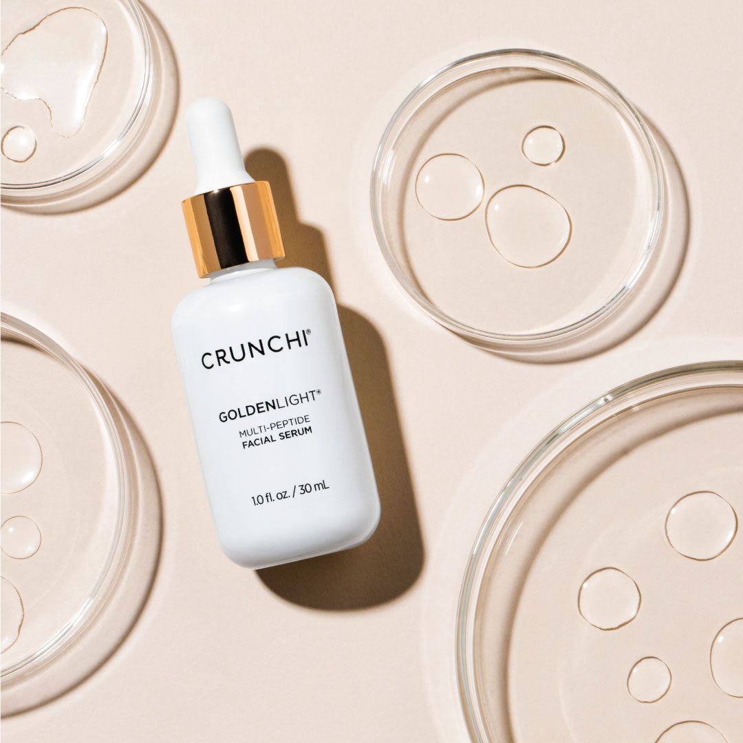 Crunchi Goldenlight Serum bottle surrounded by four product puddles in an artistic layout.