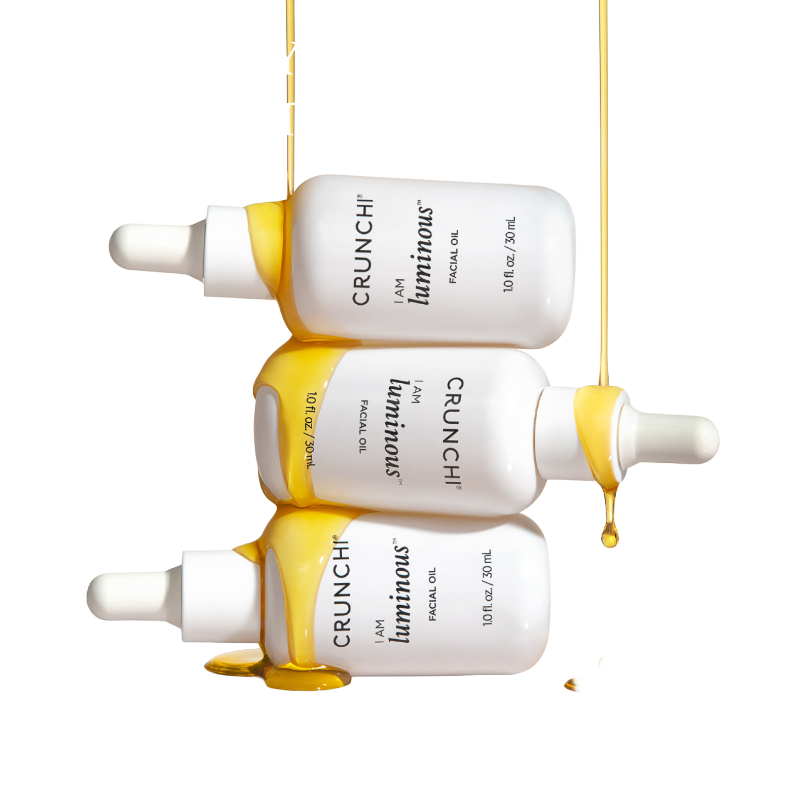 Three bottles of Crunchi I AM Luminous Facial Oil stacked horizontally, with golden oil dripping beautifully over the sides.