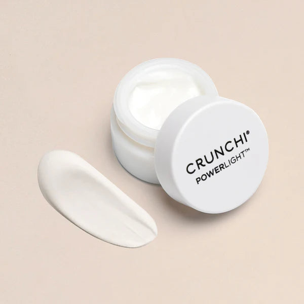 Open jar of Crunchi Powerlight Eye Cream with the lid resting beside it and a smooth product swipe next to the jar.