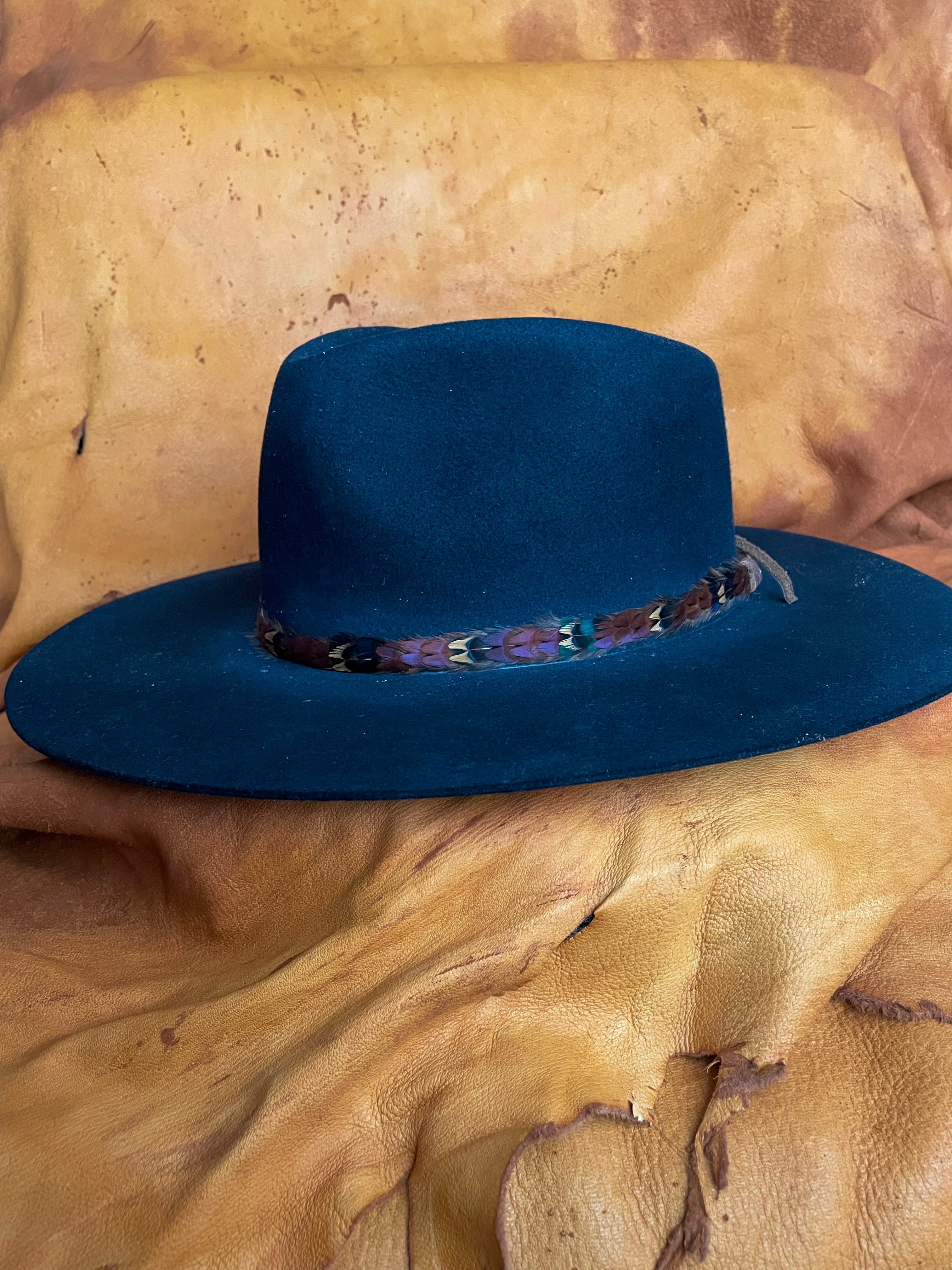 A black felt hat adorned by a pheasant feather hatband. The feathers are arranged in a repeating pattern: Maroon, Gold, Emerald. 