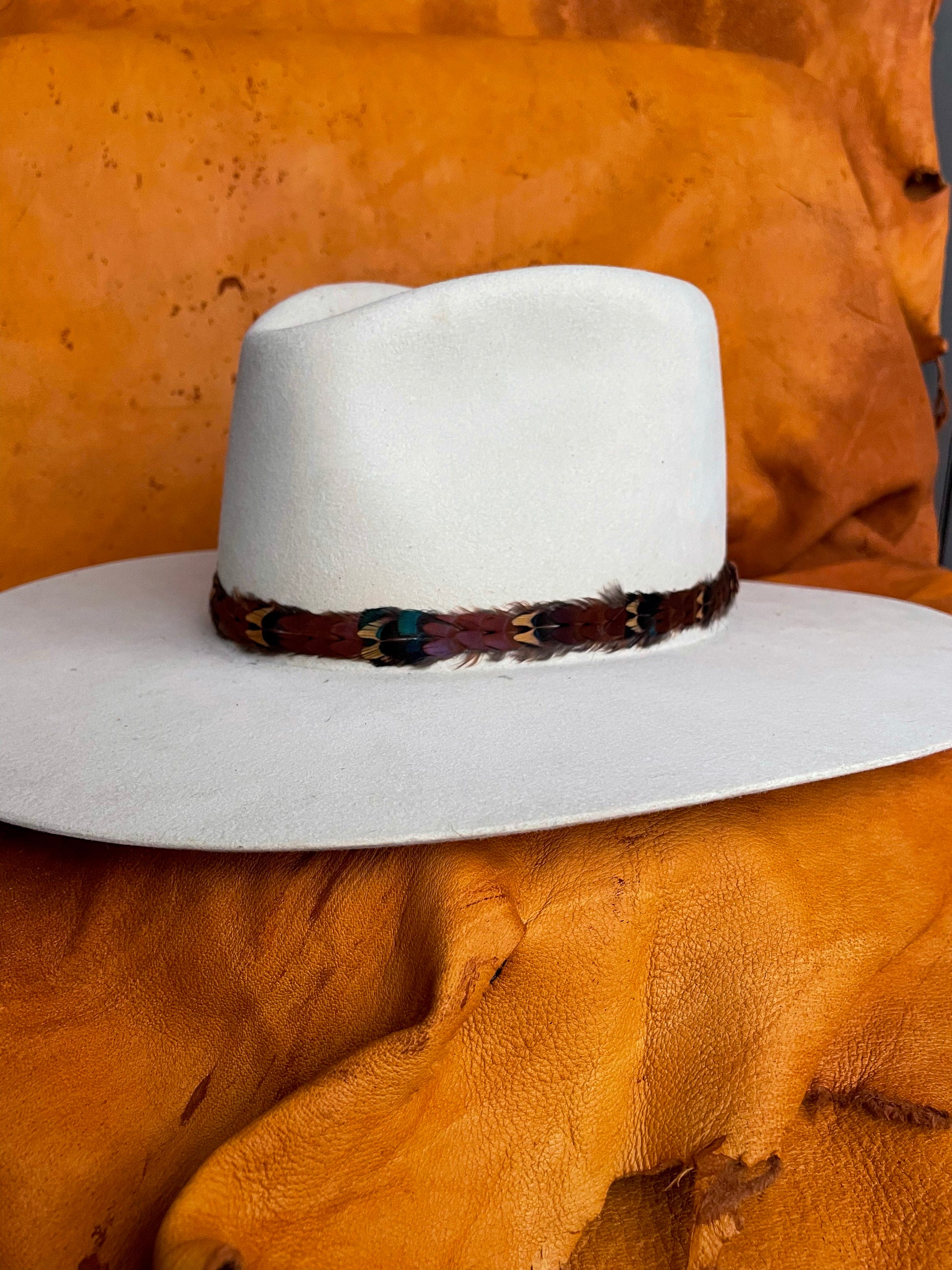 A maroon, gold, emerald patterned pheasant feather hatband on an ivory felt hat. 
