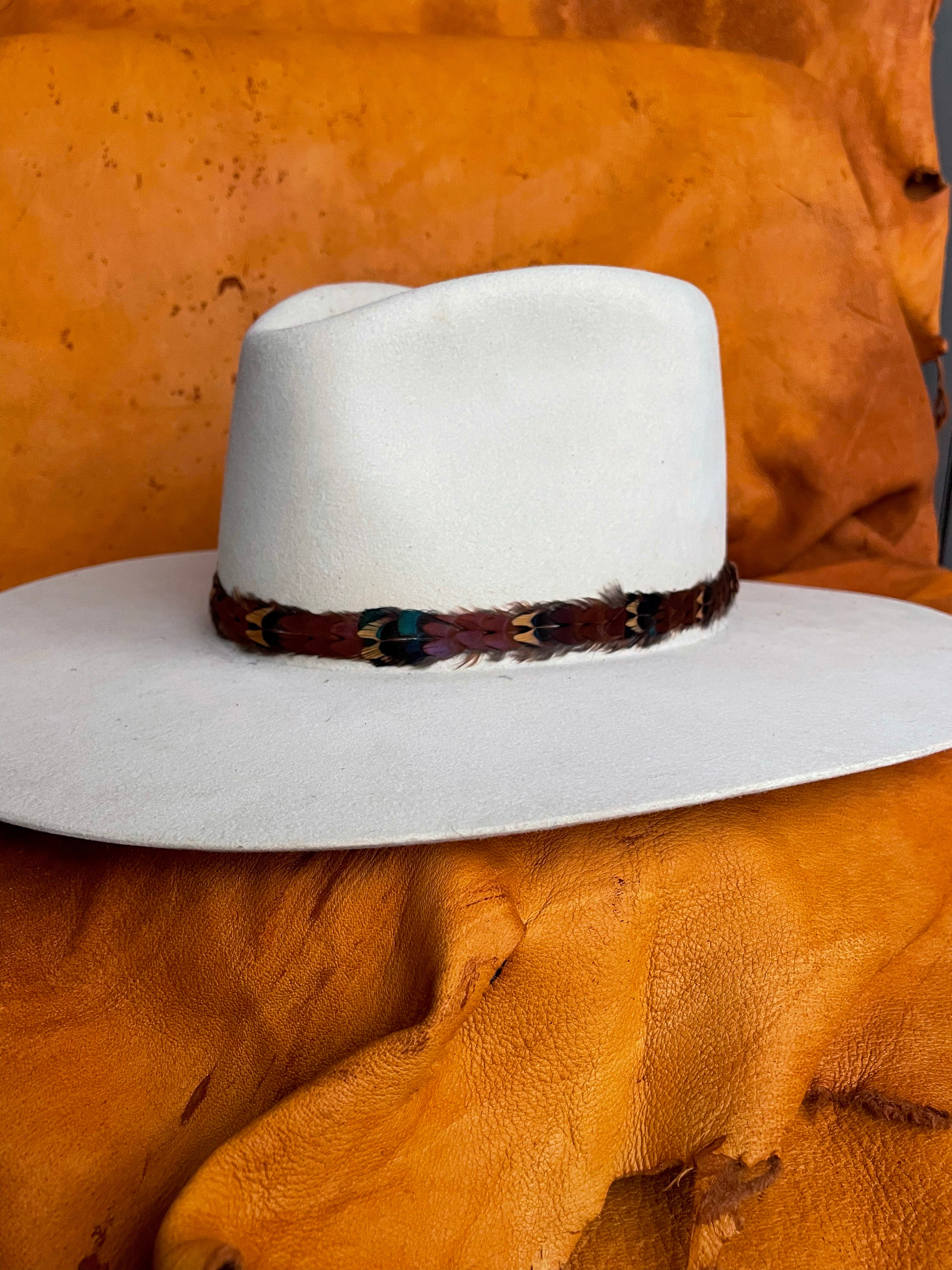 A maroon, gold, emerald patterned pheasant feather hatband on an ivory felt hat. 