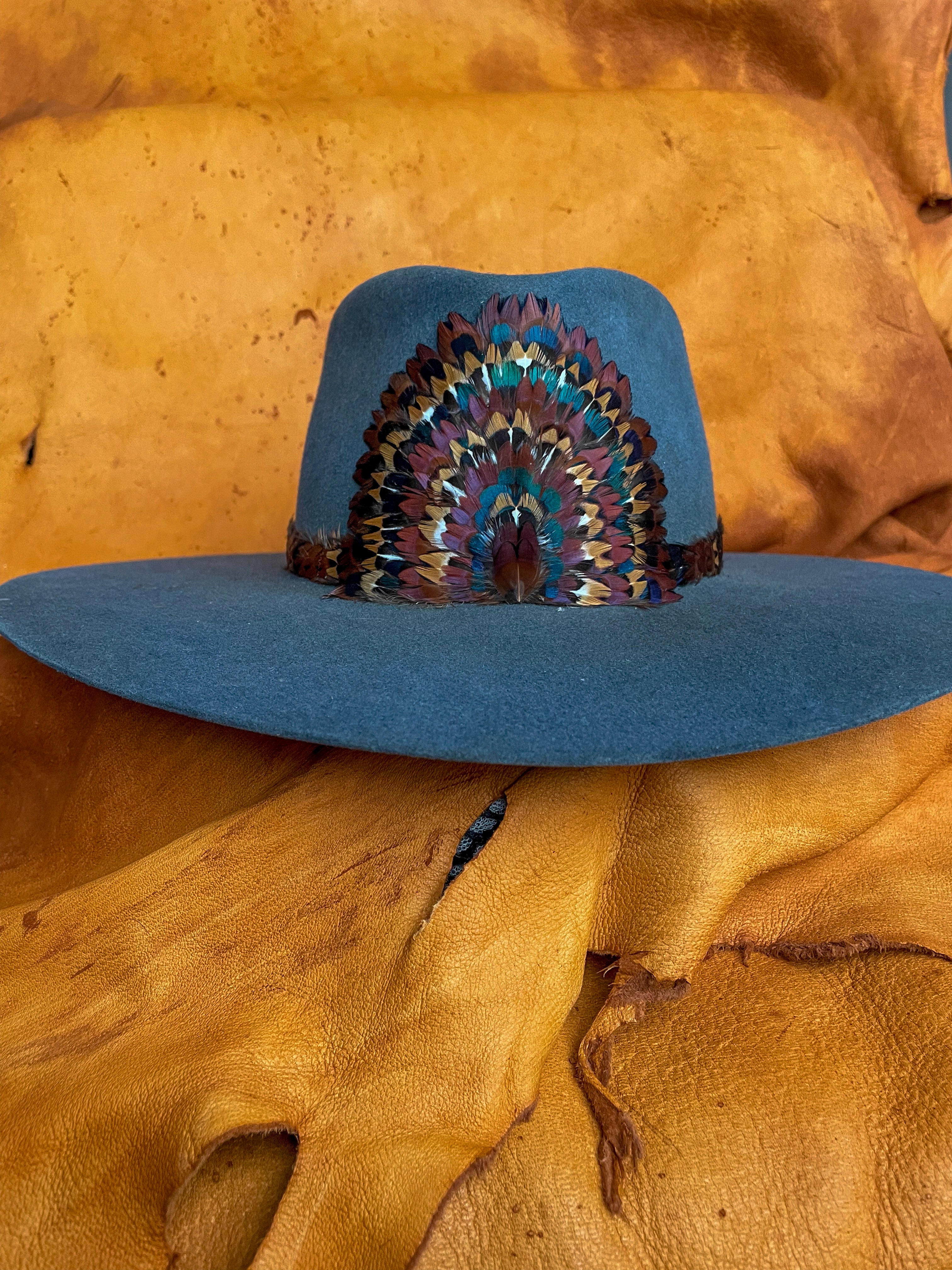 A front view of a handcrafted hatband and removable feather medallion built from the iridescent neck feathers of a wild rooster pheasant on a steel blue felt hat.