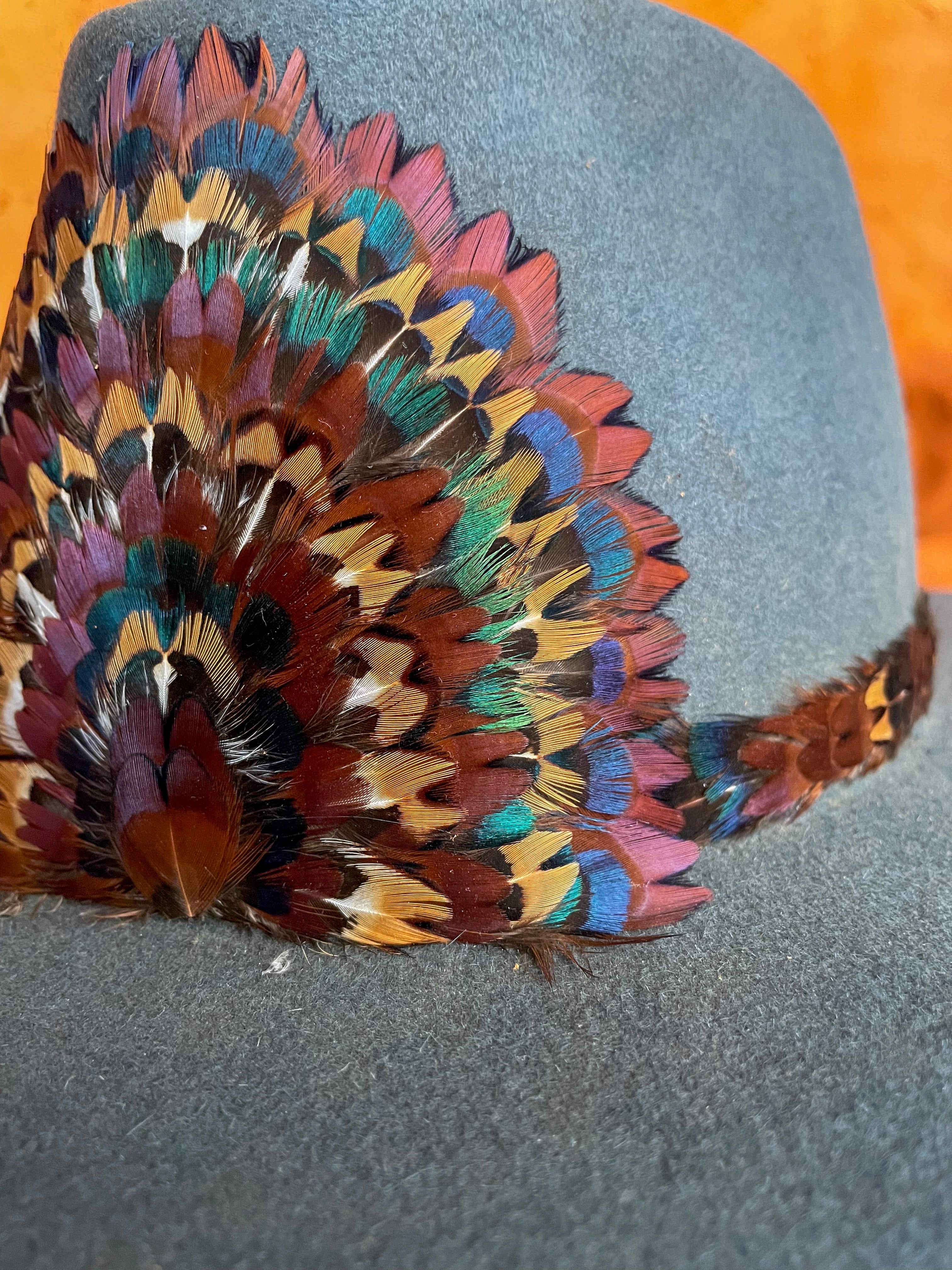 A close up angle view of a handcrafted hatband and removable feather medallion built from the iridescent neck feathers of a wild rooster pheasant on a steel blue felt hat.