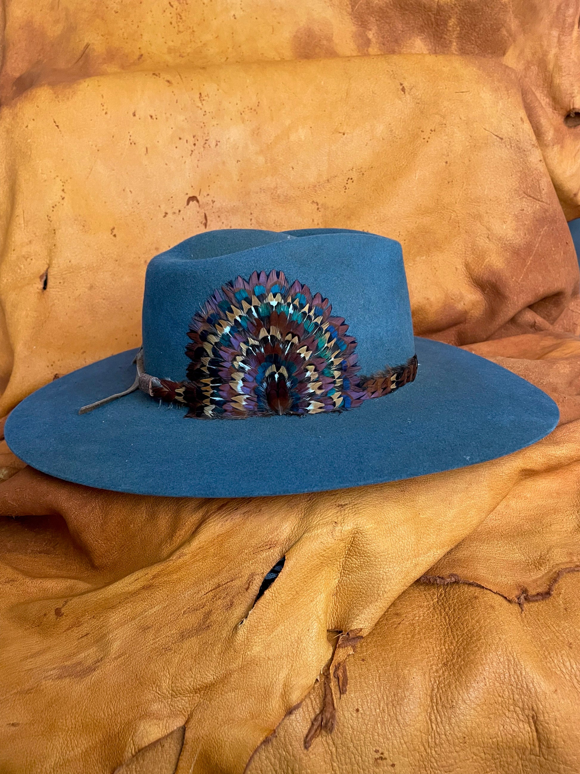 A side view of a one of a kind hatband and removable feather medallion on a steel blue felt hat.