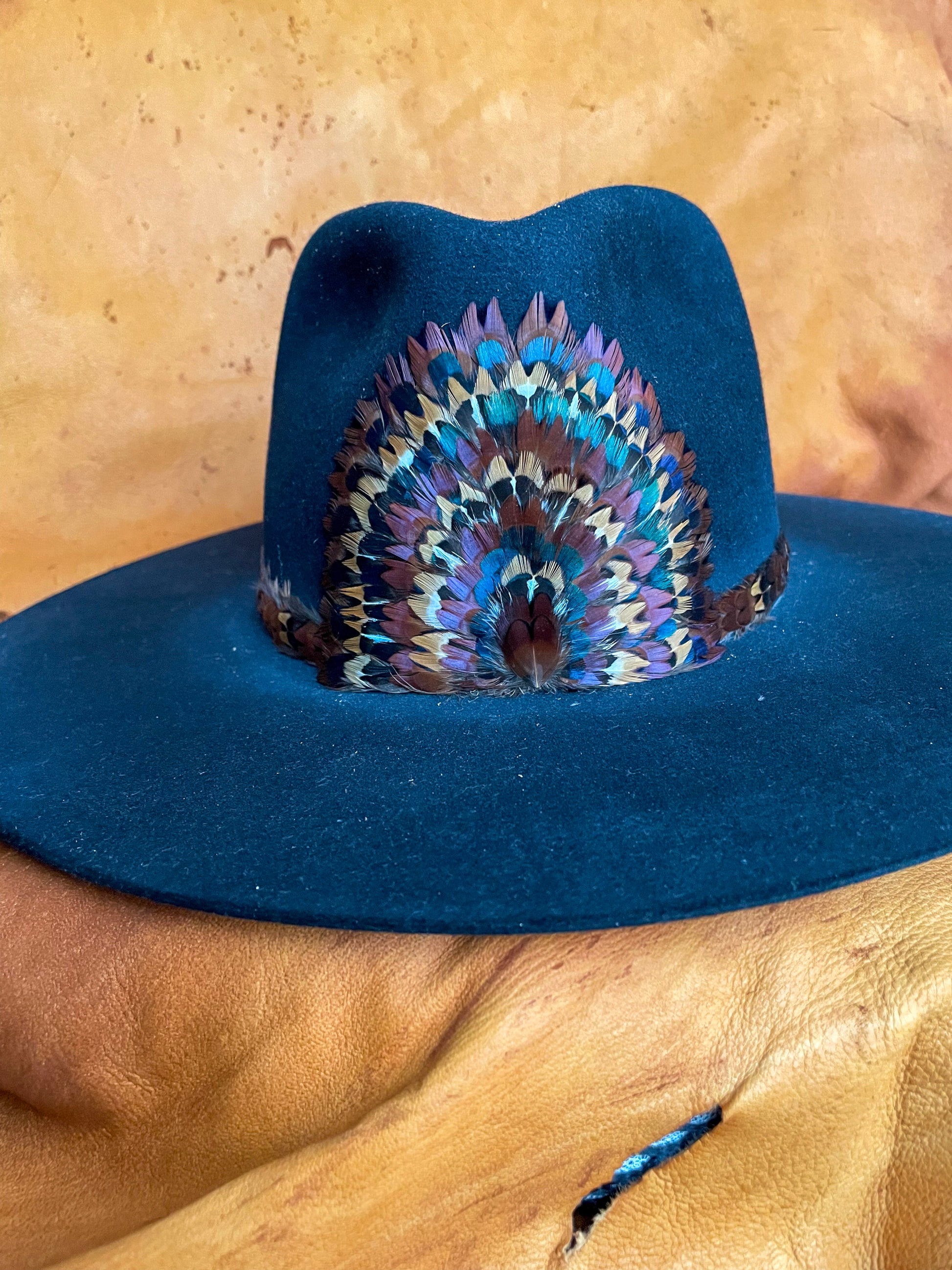 A front view of a one of a kind hatband and removable feather medallion on a black felt hat.