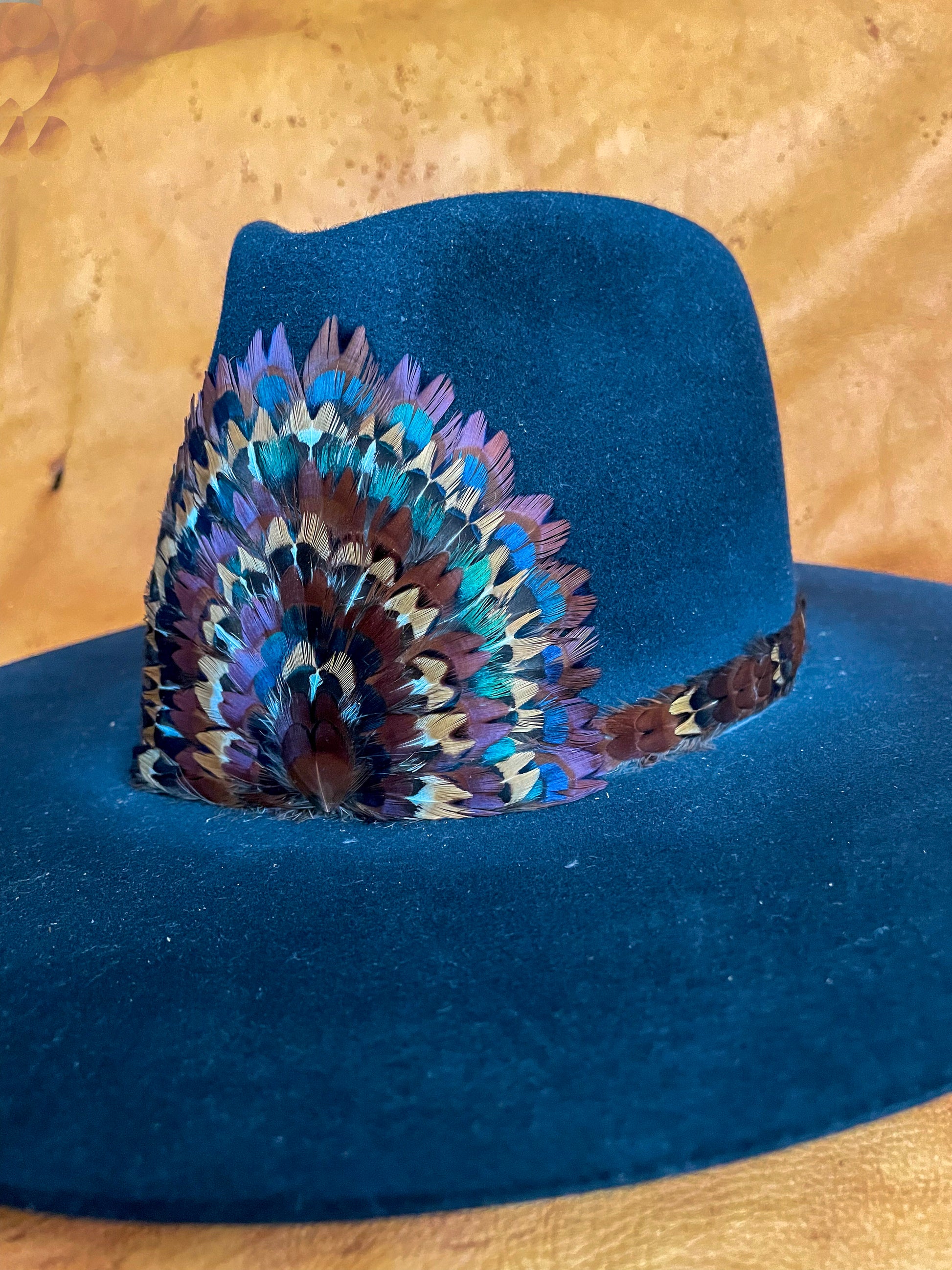 An angled view of a one of a kind hatband and removable feather medallion on a black felt hat.