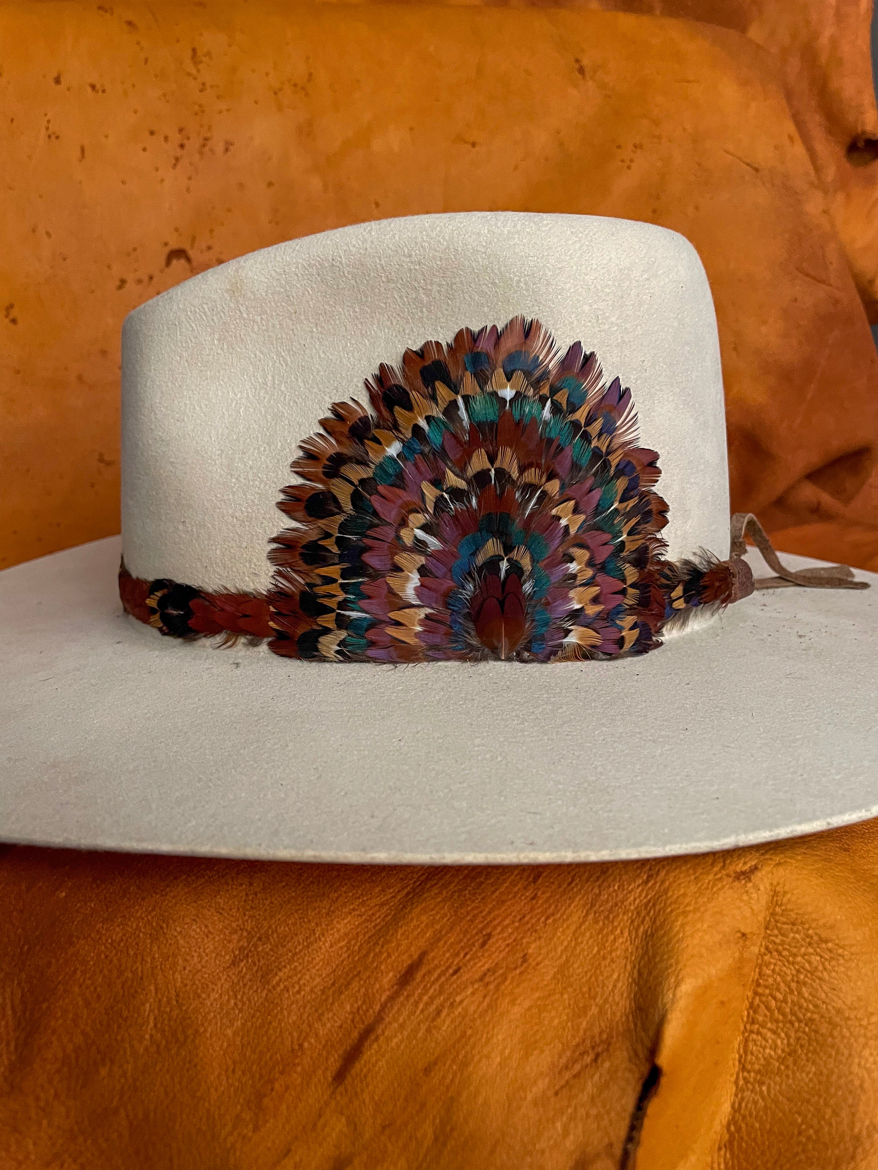 A side view of a one of a kind hatband and removable feather medallion on an ivory felt hat.