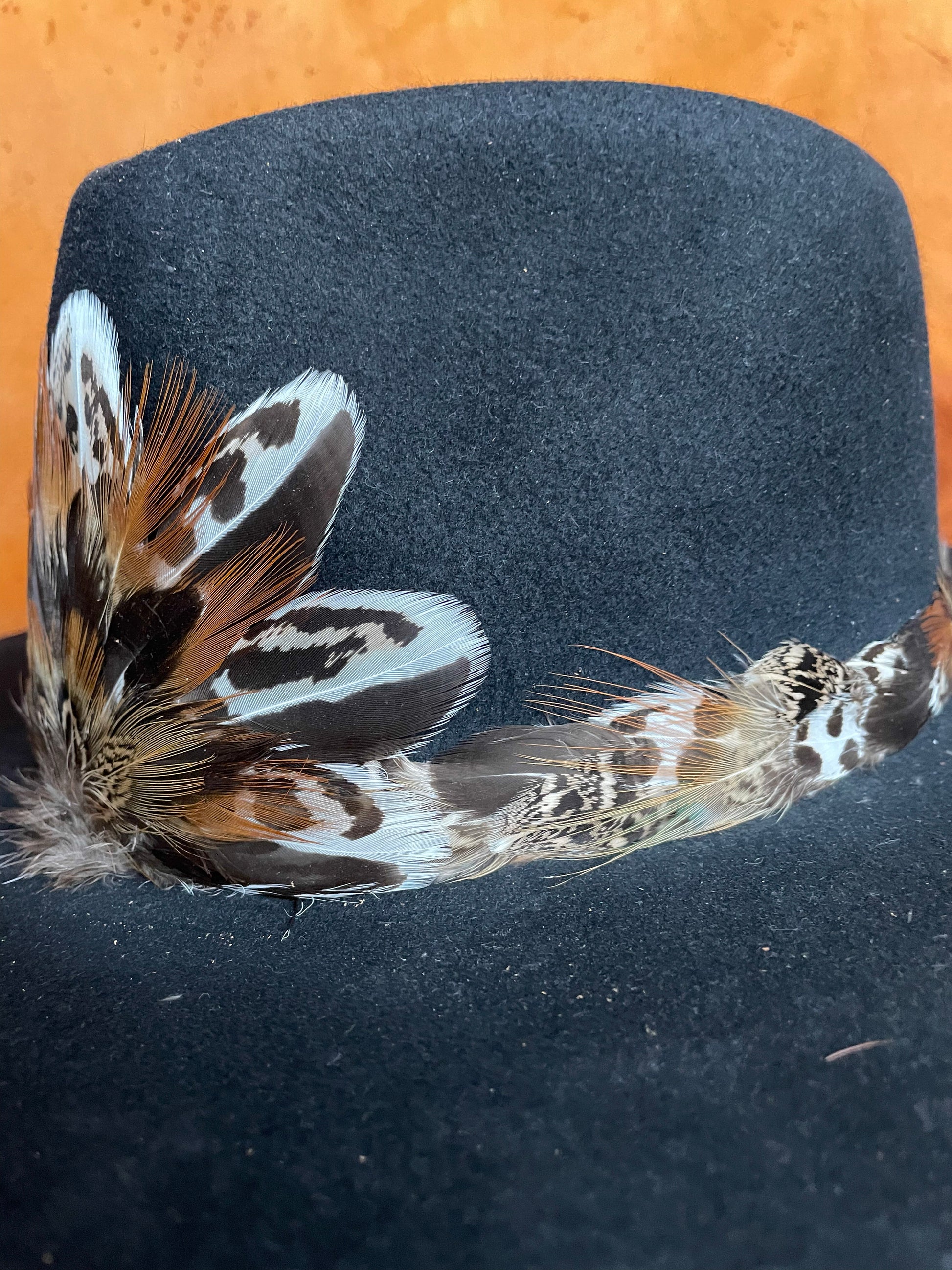 Up close and angle view of a Sage Grouse and Pheasant feather hatband and matching magnetic medallion on the front of a black felt hat.