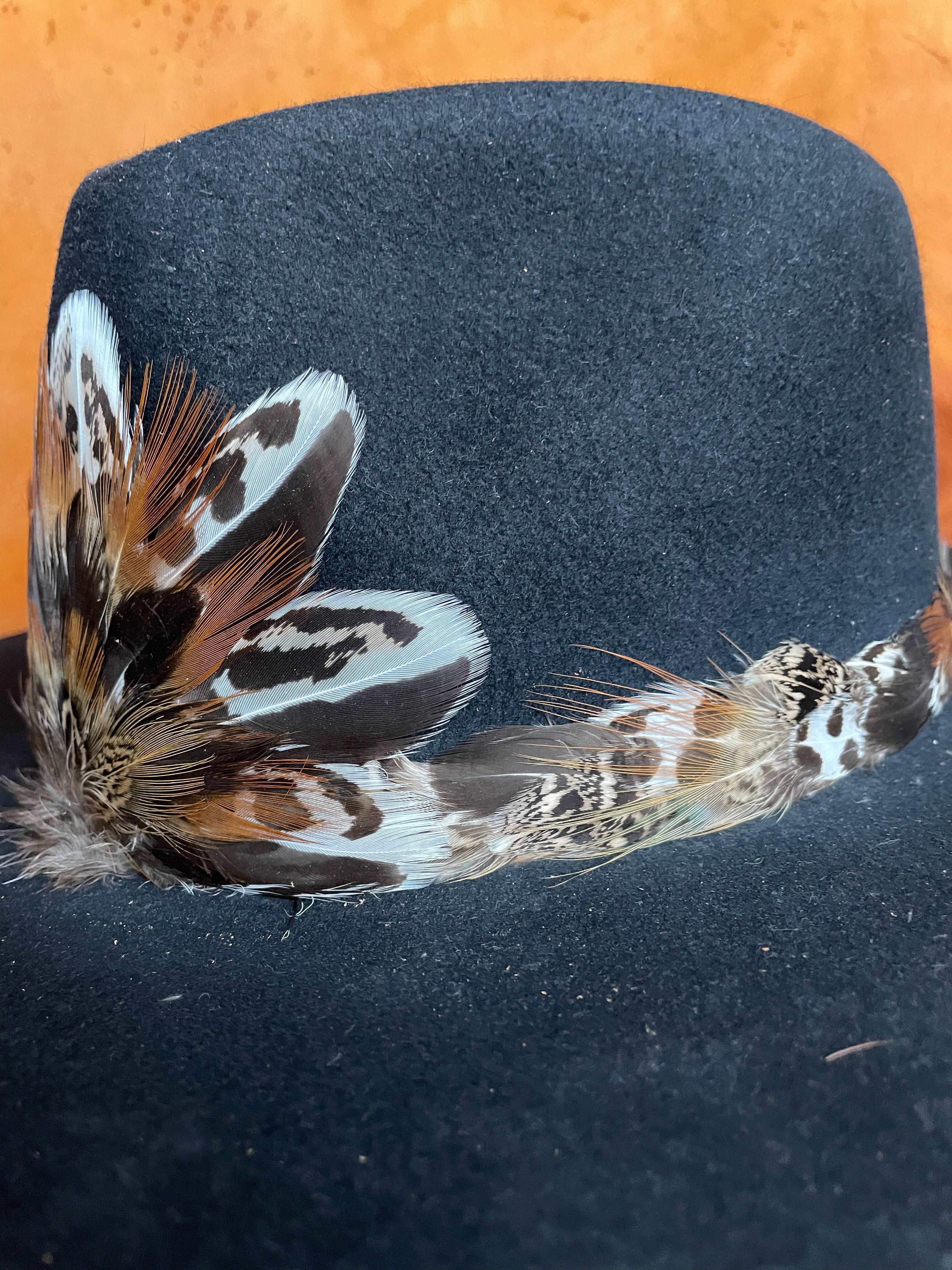 Up close and angle view of a Sage Grouse and Pheasant feather hatband and matching magnetic medallion on the front of a black felt hat.