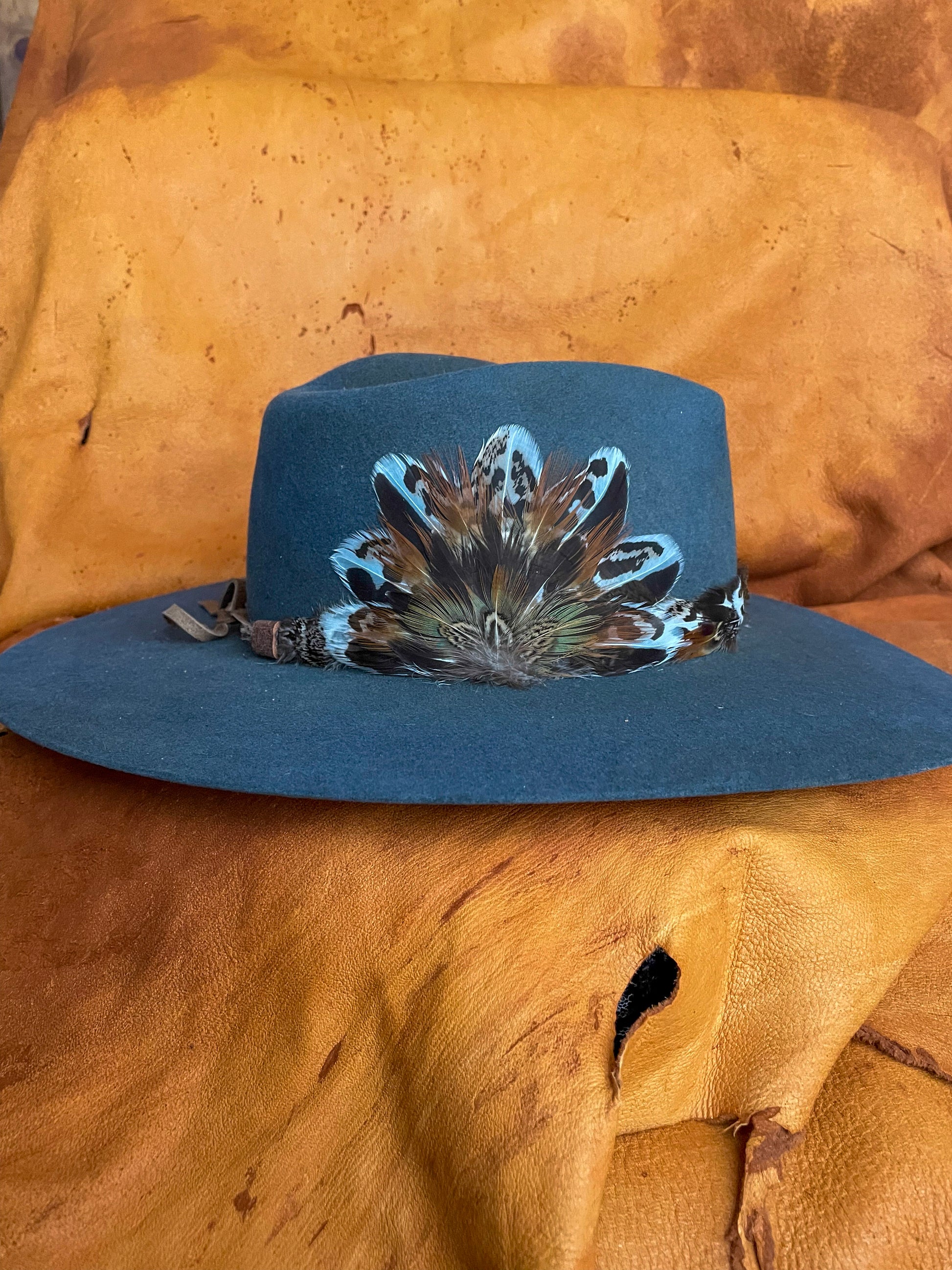 Removable magnetic medallion with mixed upland bird feathers on the side of a steel blue felt hat.