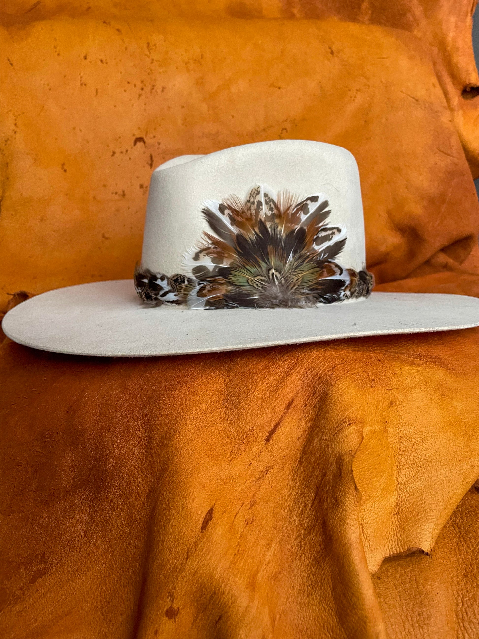 Handmade feather hatband with sage grouse and pheasant feathers in earthy tones with pops of rust and a matching removable magnetic medallion.