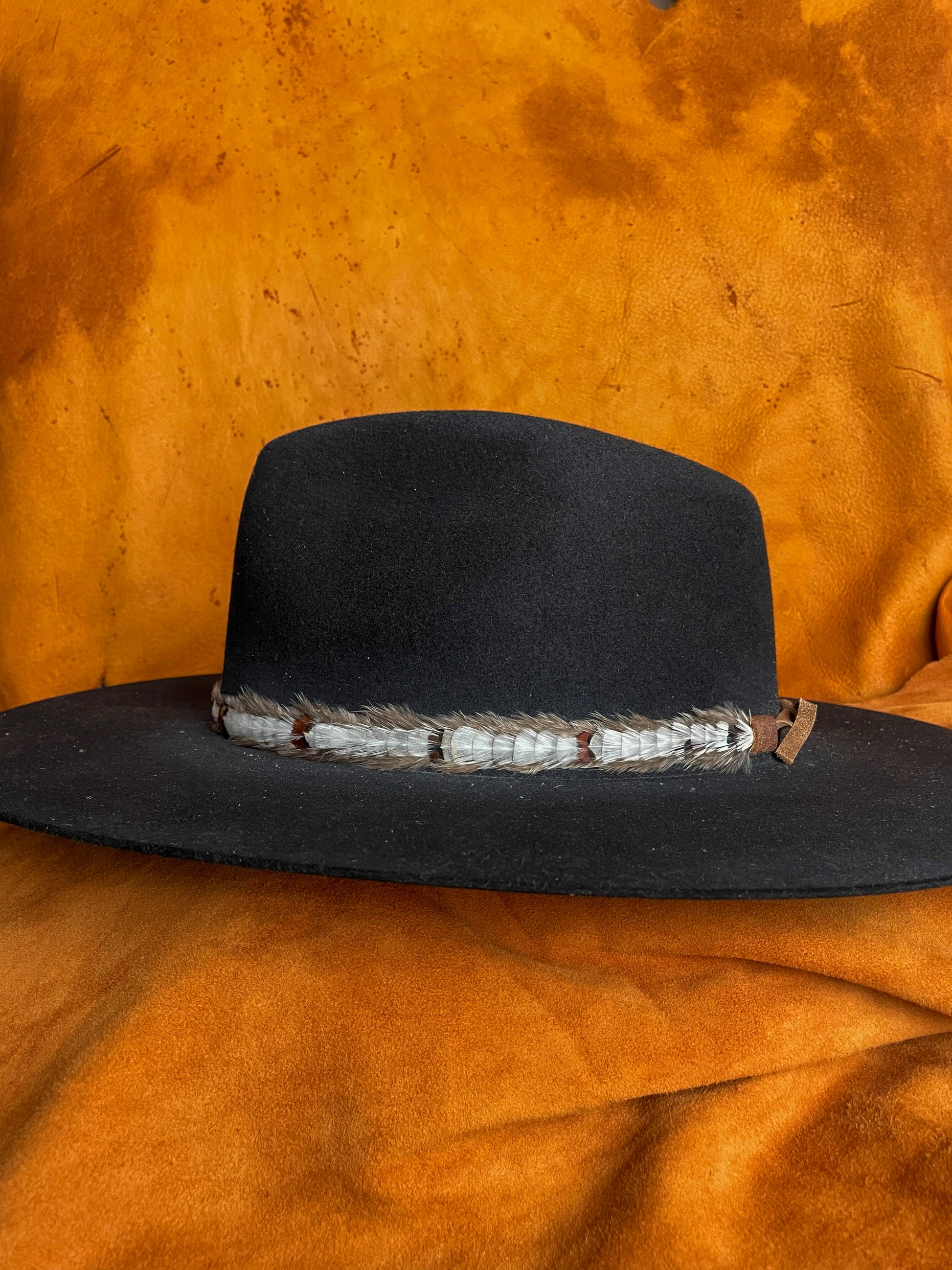Handmade white feather hatband with subtle patterned accents on a black felt hat. 