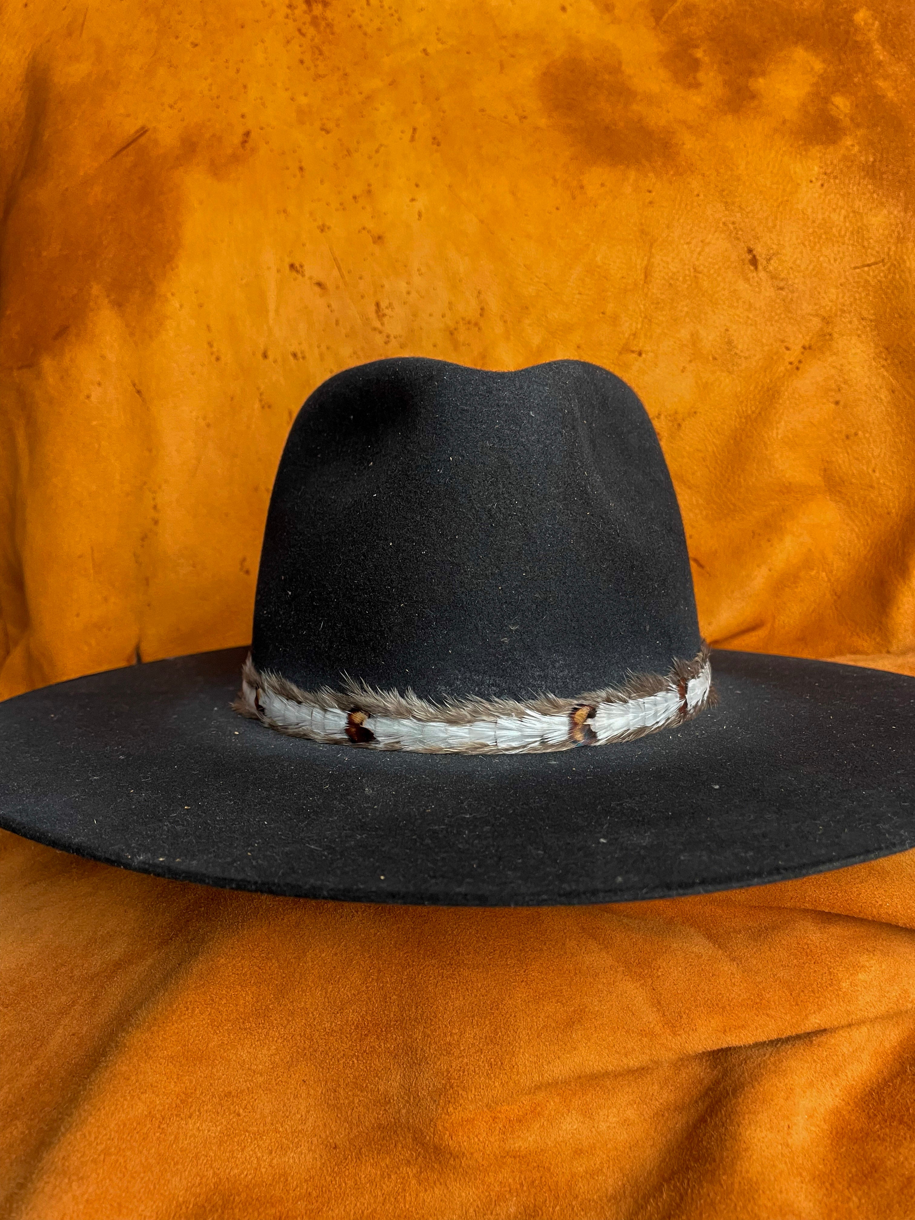 Delicate feather hatband with small patterned details on a black felt hat. 
