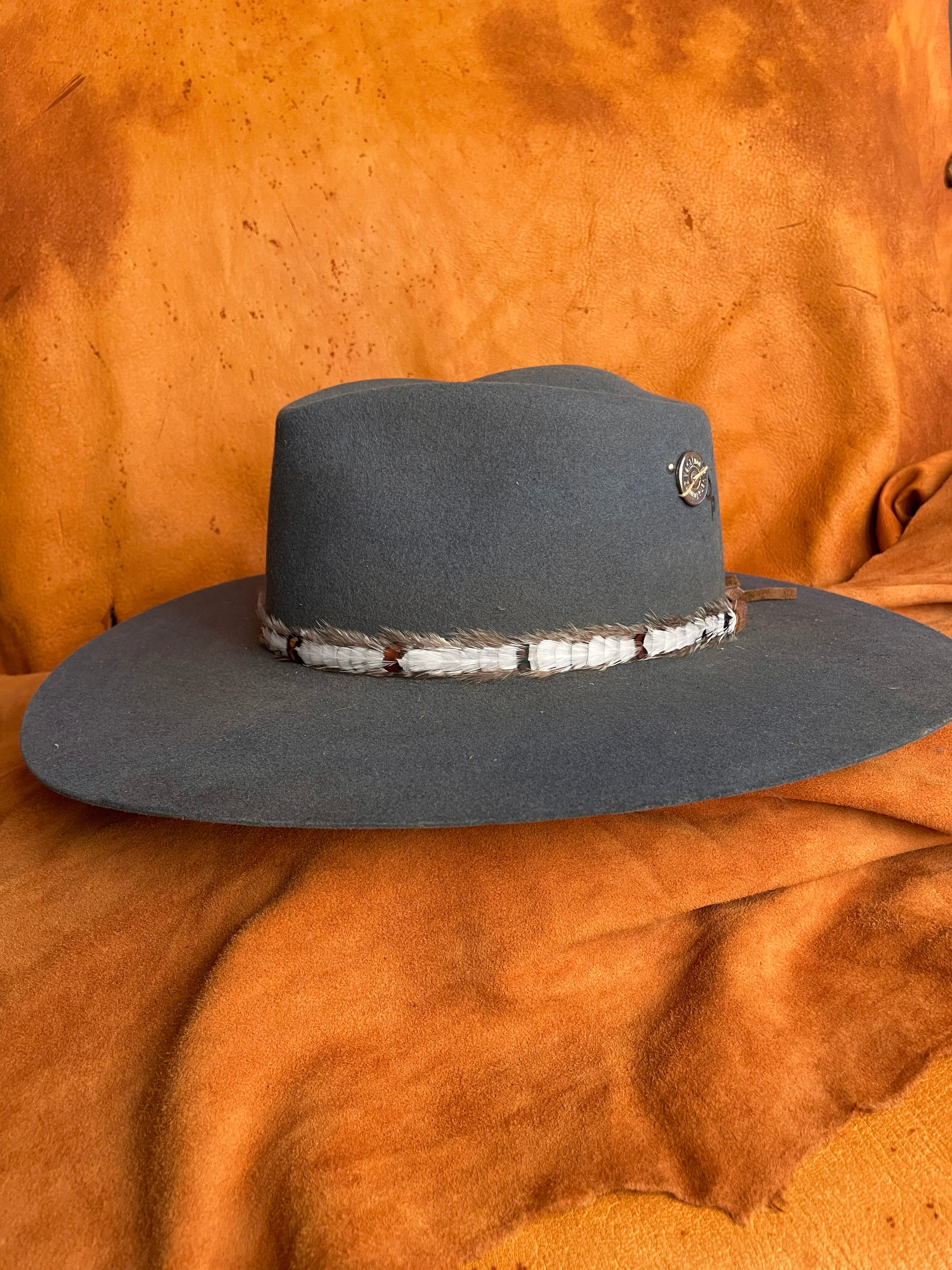 Side view of clean and simple feather hatband with small patterned details on a steel blue felt hat. 