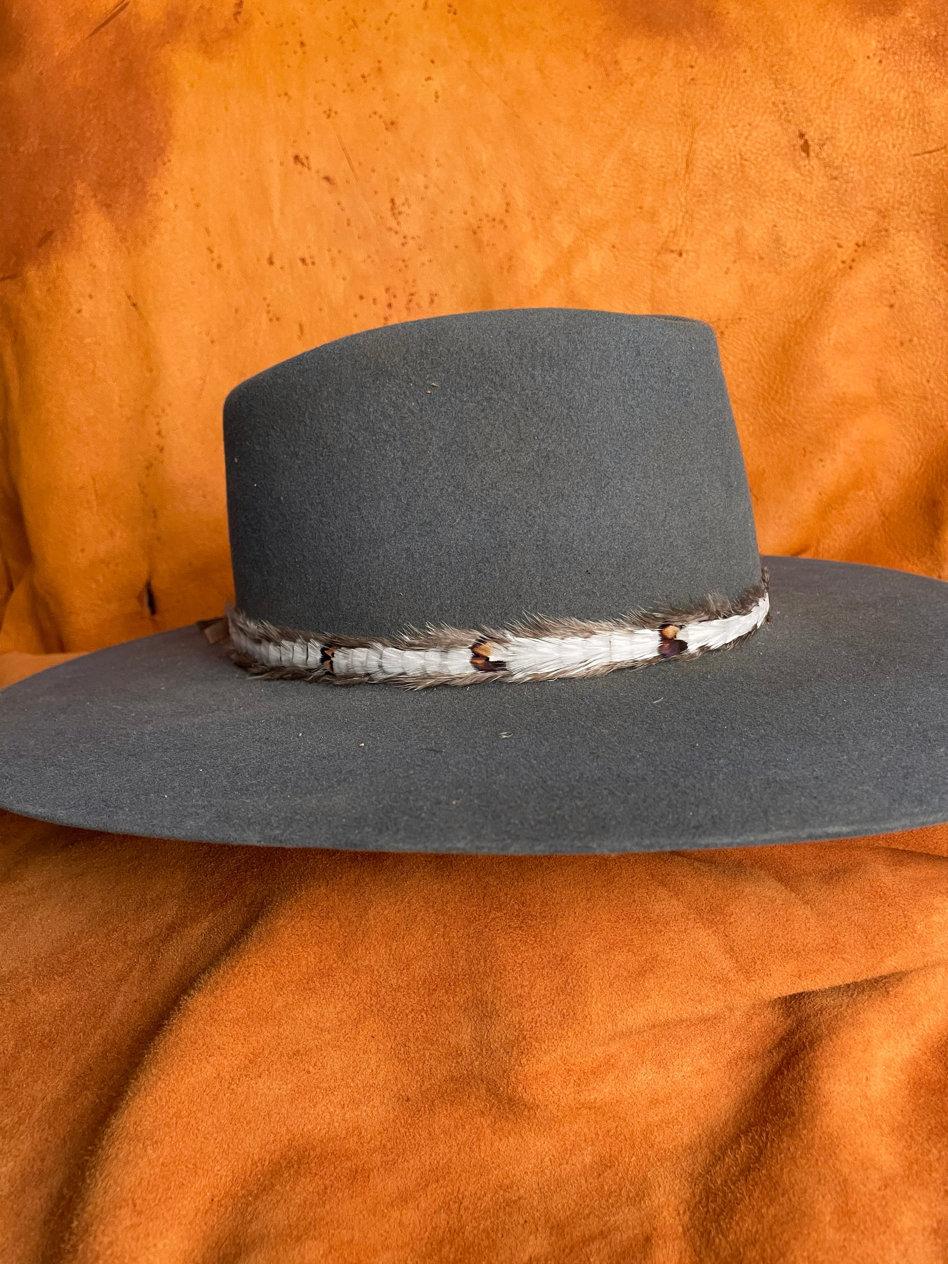 Side view of a steel blue felt hat showcasing a handmade white feather hatband with subtle patterned accents.