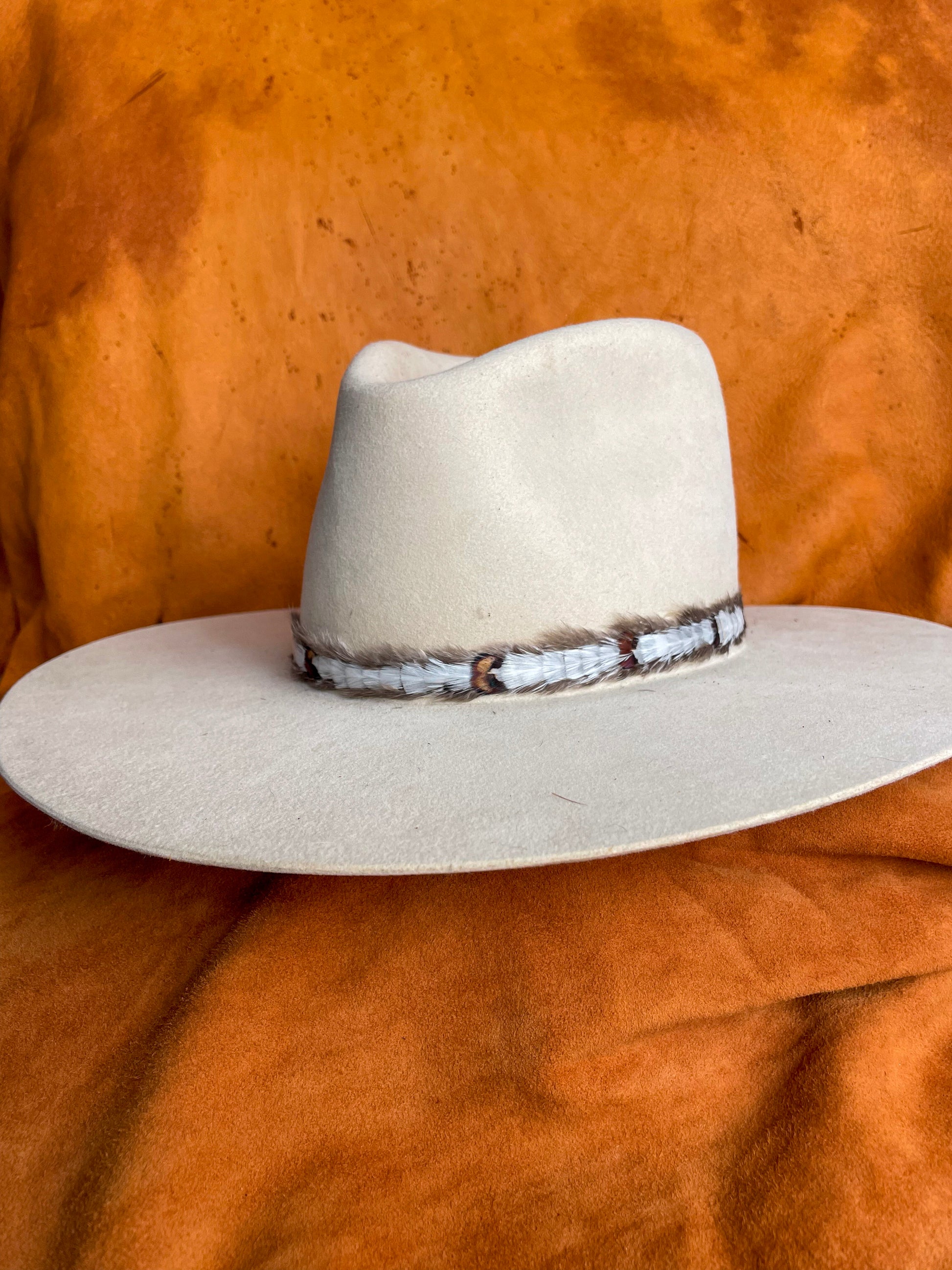 Front angle of a cream felt hat with a handmade white feather hat band. 