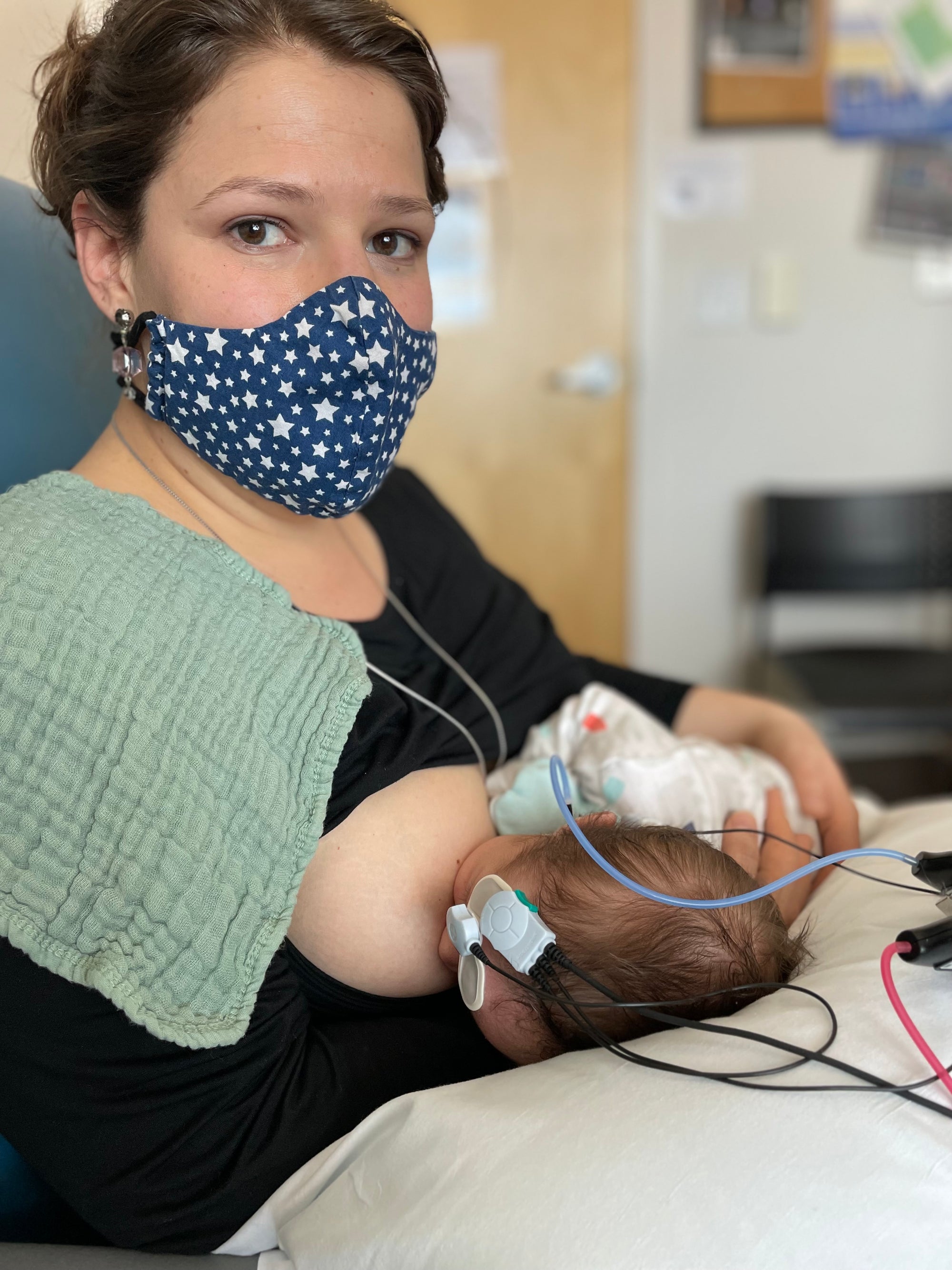 motional moment of Olivia Poyer holding and nursing her two-month-old son during an audiology appointment. He is connected to testing wires confirming his deafness, while Olivia looks into the camera with quiet strength and love.