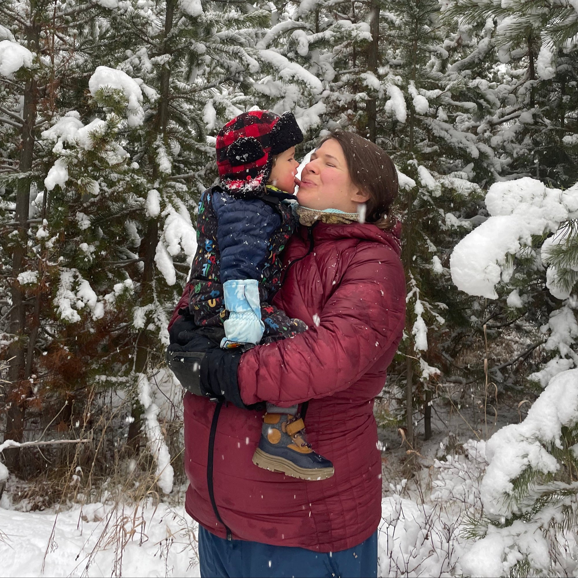 Olivia Poyer holding her son Bode in a snowy pine forest just weeks before her daughter’s birth — snow falling softly as she balances motherhood, anticipation, and gratitude.