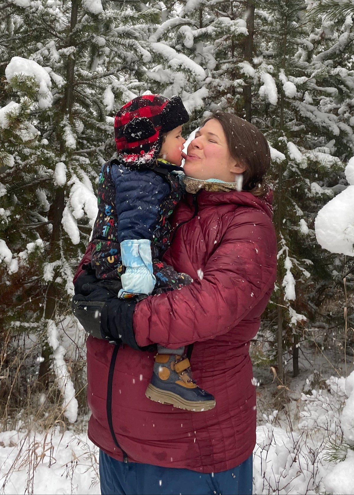 Olivia Poyer holding her son Bode in a snowy pine forest just weeks before her daughter’s birth — snow falling softly as she balances motherhood, anticipation, and gratitude.