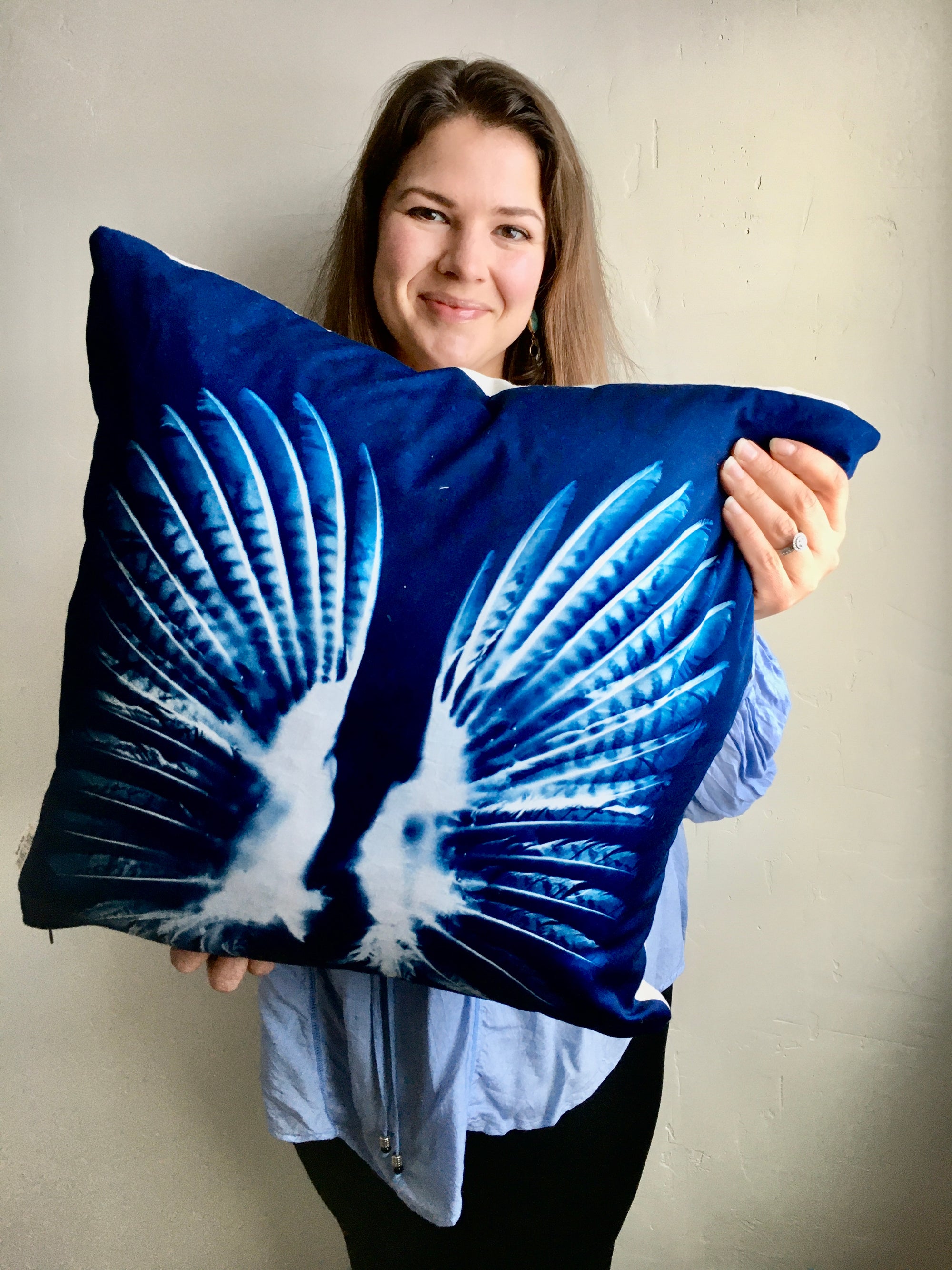 Olivia Poyer in 2020 holding one of her first cyanotype pillow covers, featuring a pheasant wing print in flight — a reflection of her early creative journey from upholstery to intentional art.