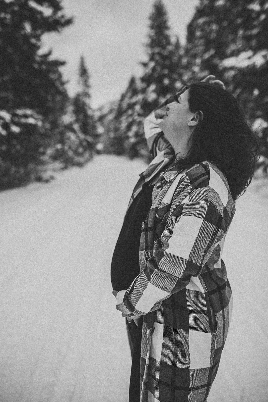 Black-and-white photo of Olivia Poyer standing on a snowy mountain road, hand on her pregnant belly and head tilted back in peaceful reflection — symbolizing strength, surrender, and motherhood.