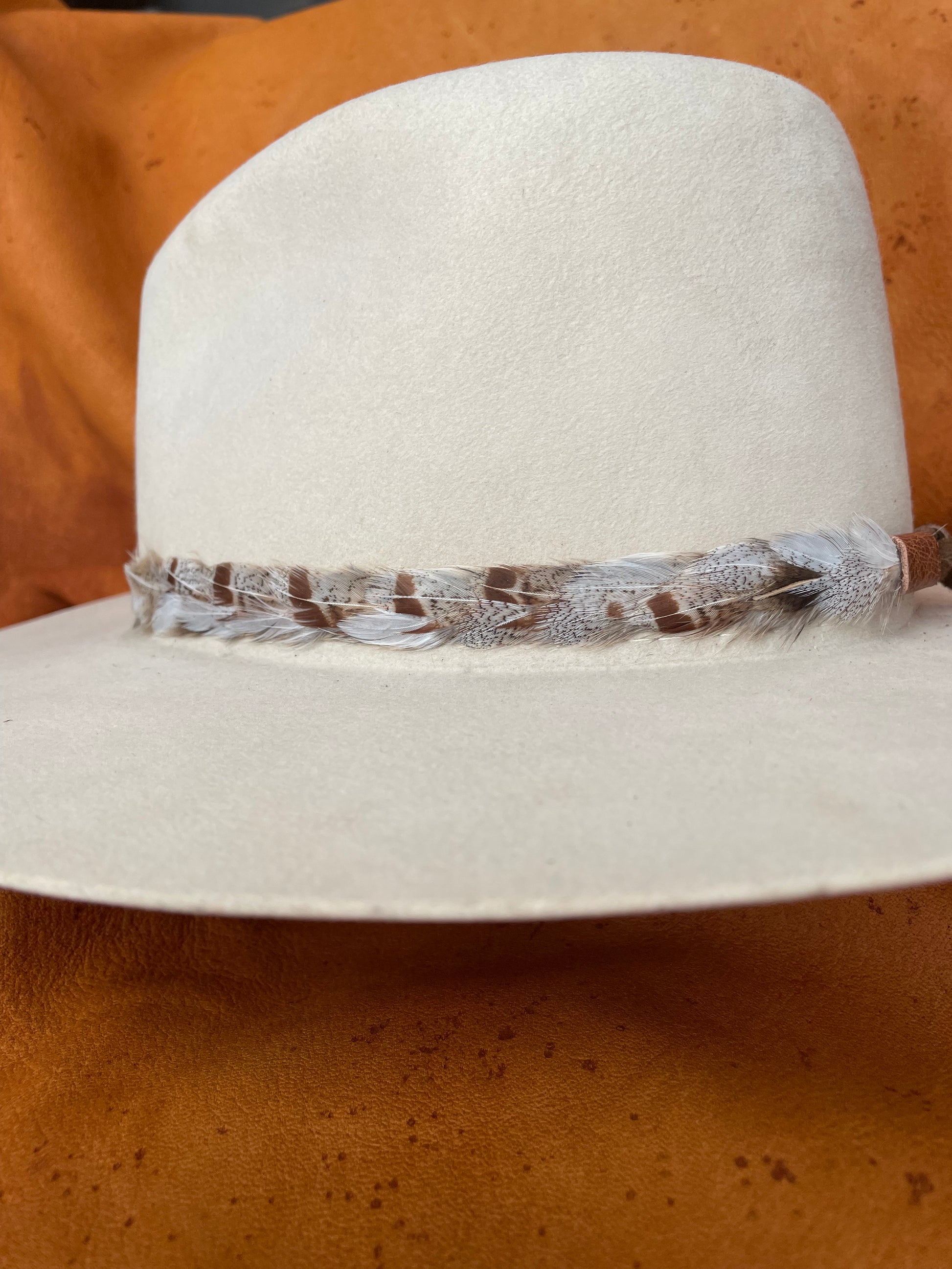 Handcrafted feather hatband with leather ties on cream hat, side-back angle”