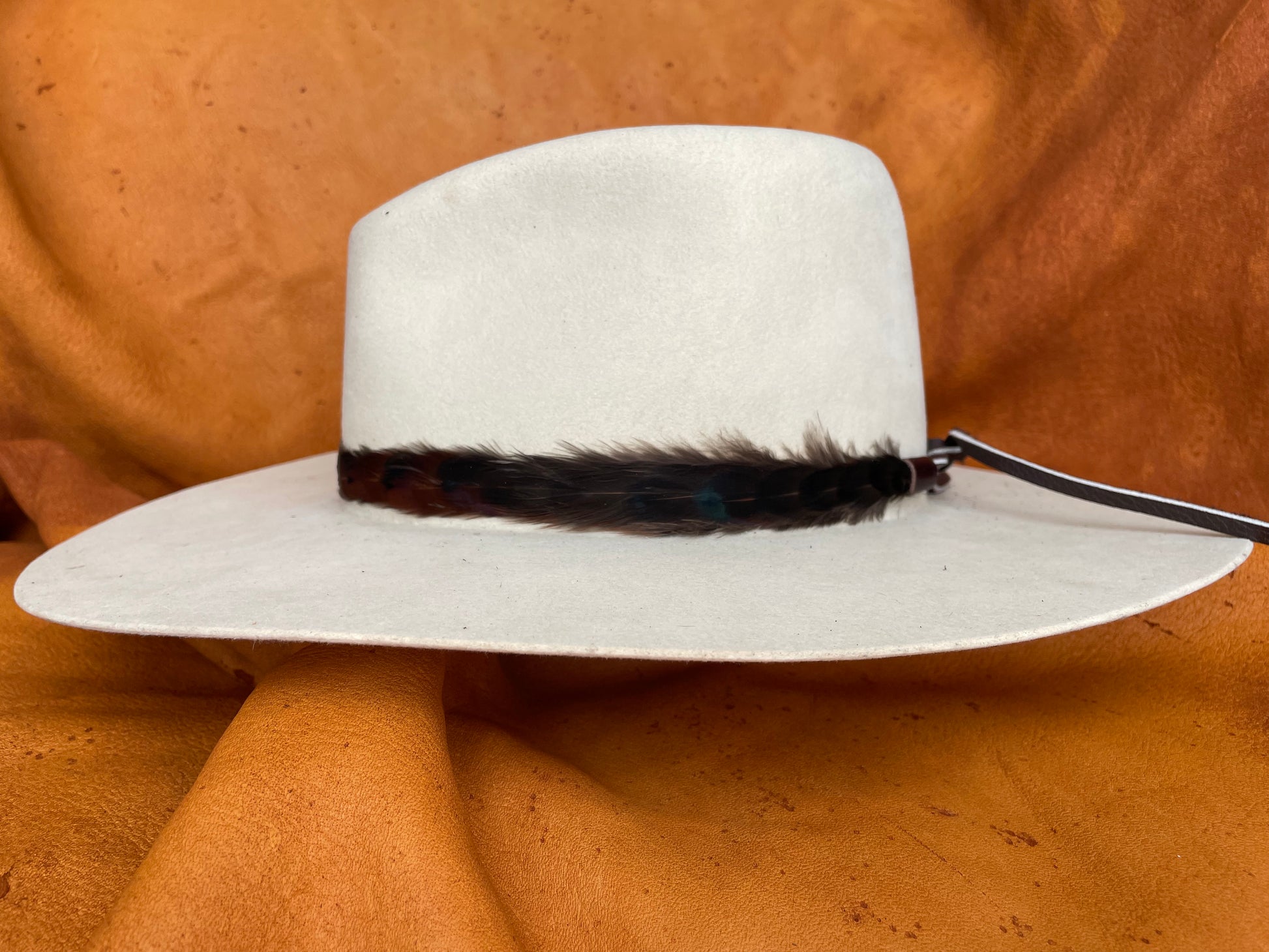 Side view of black feather hatband on cream hat