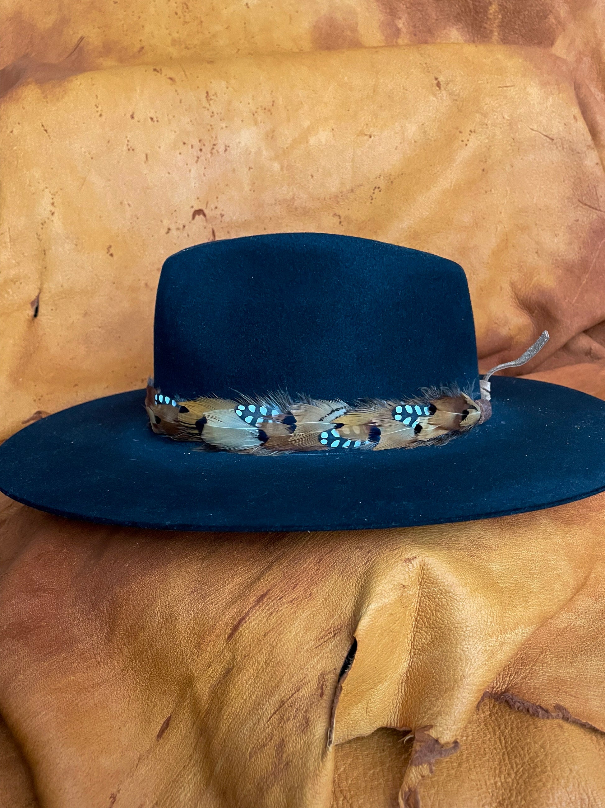 Handmade feather hatband with golden pheasant and quail feathers with black polka dot accents on a black felt hat sideview.
