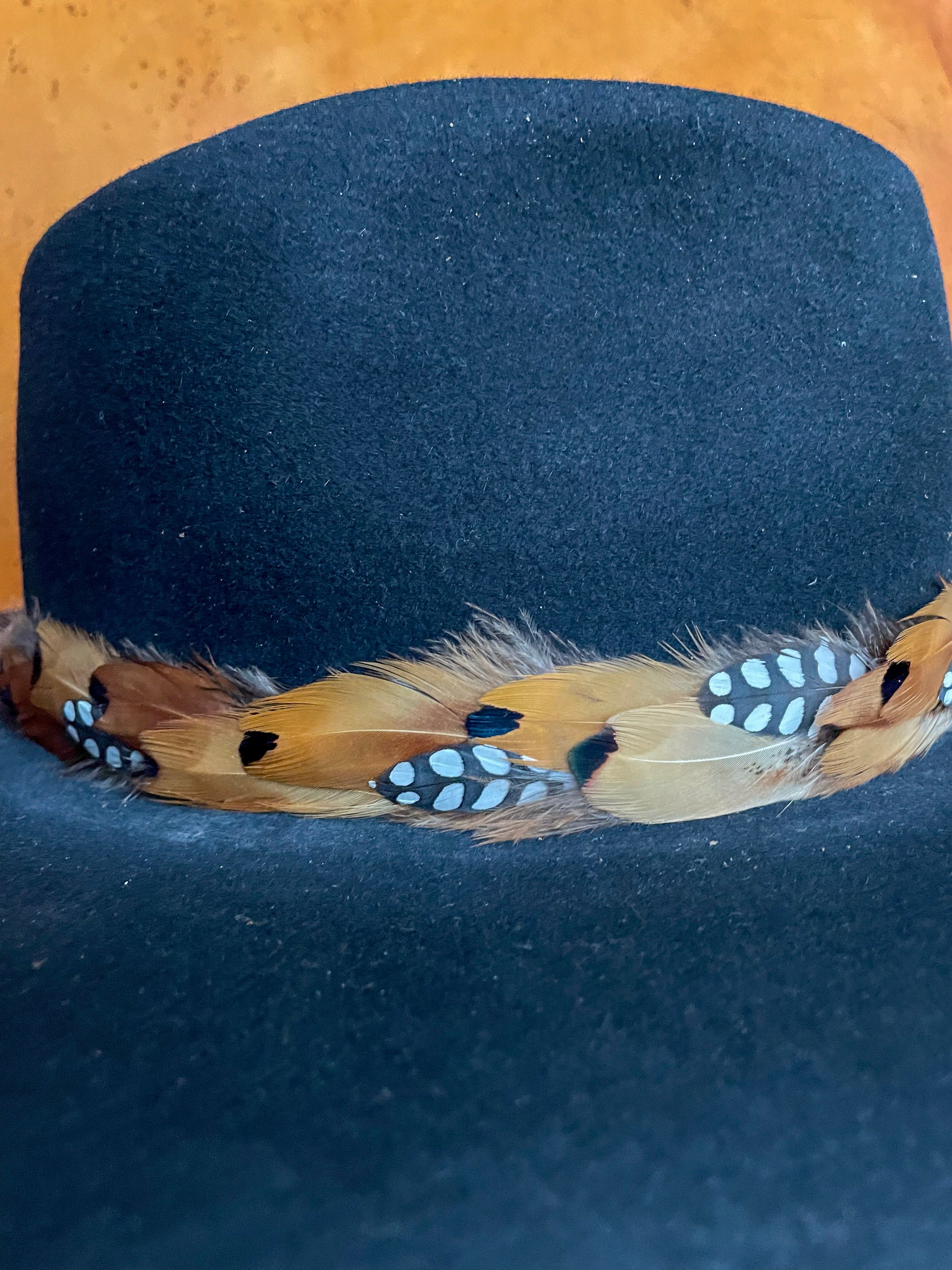 Close-up of yellow and copper pheasant feathers with spotted quail feather detail on a black felt hat.