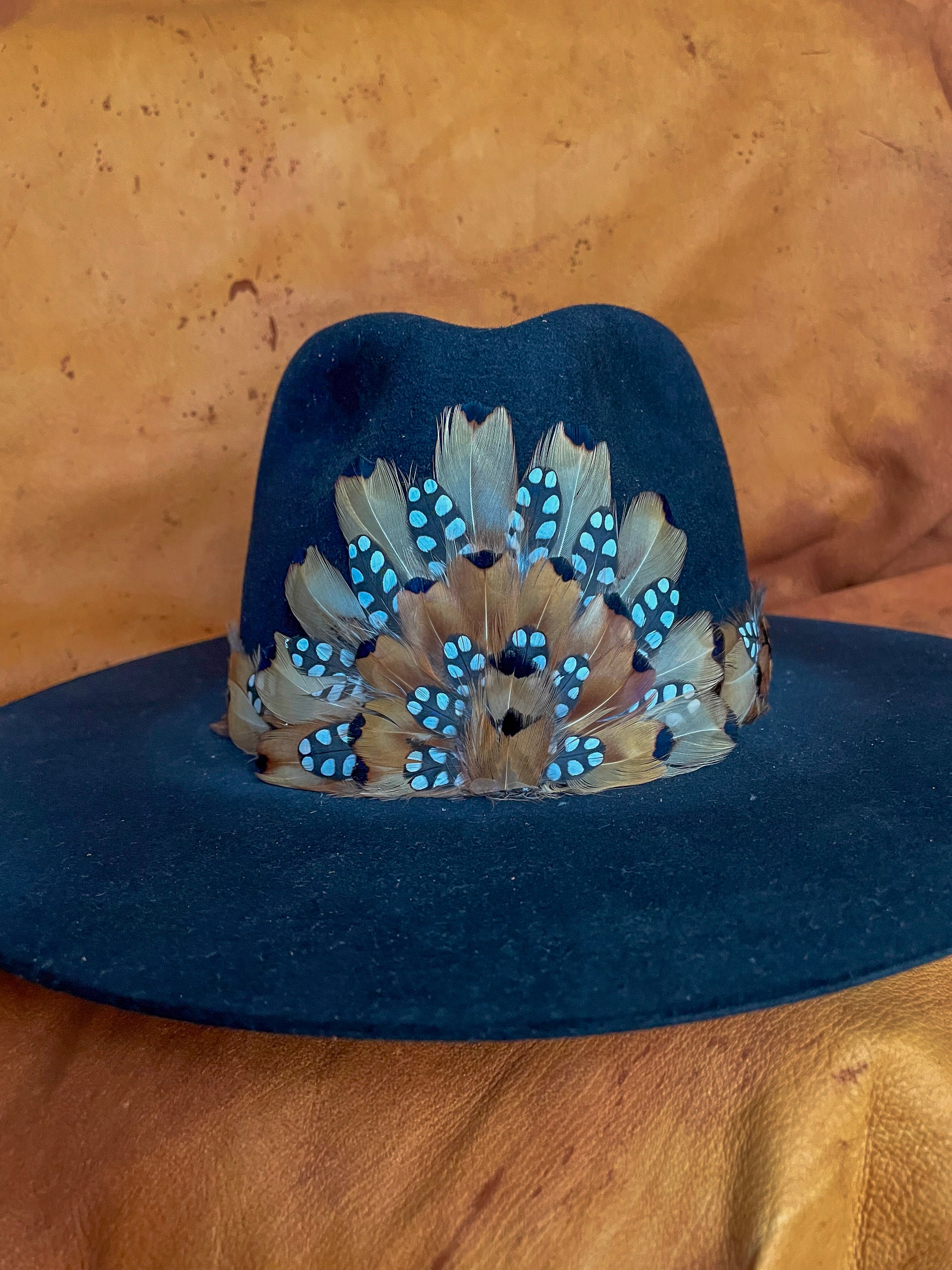 Handmade feather hatband and medallion with golden pheasant and quail feathers with black polka dot accents,
styled on a black felt hat.