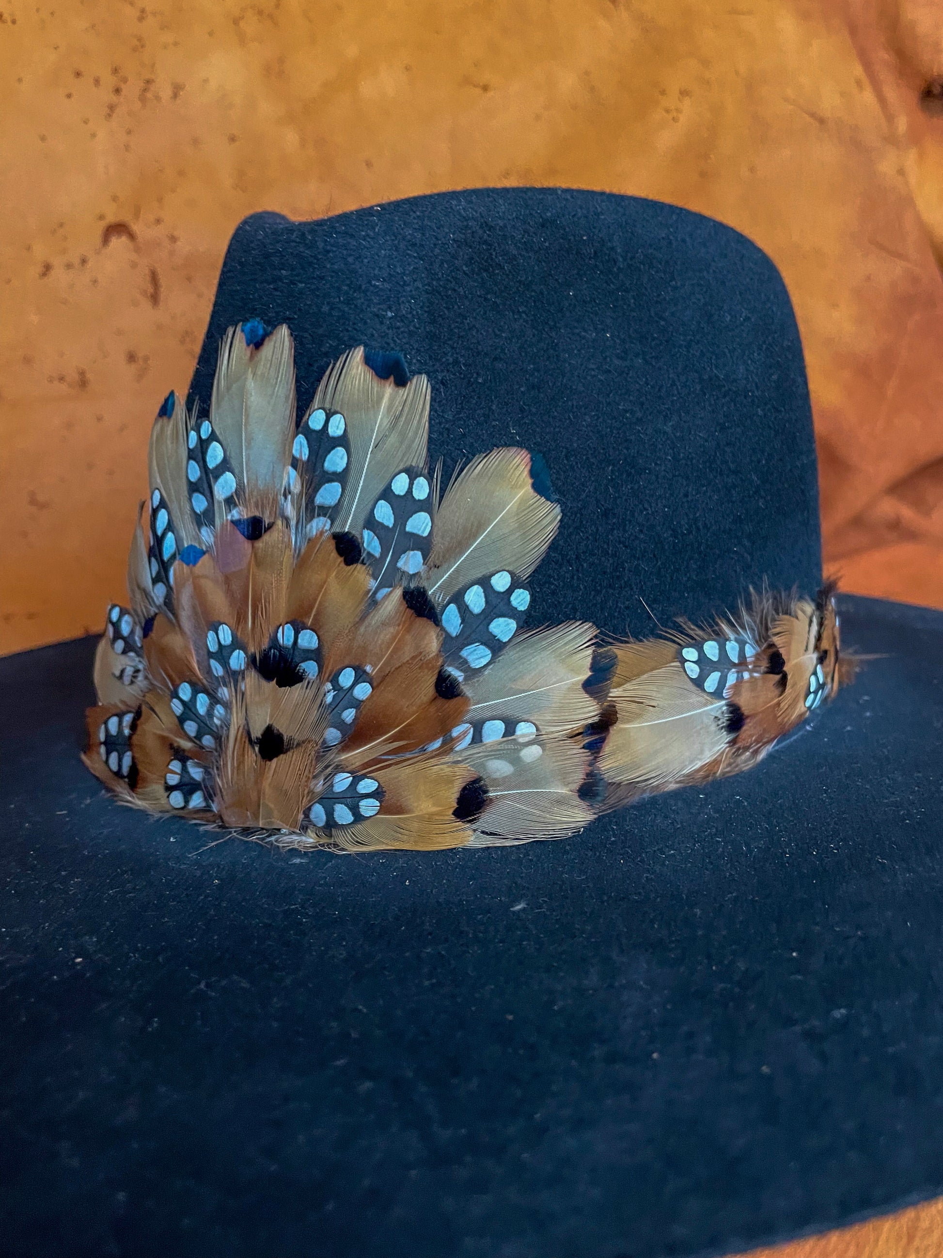 Diagonal view of a handmade feather hatband and medallion with golden pheasant and quail feathers with black polka dot accents,
styled on a black felt hat.