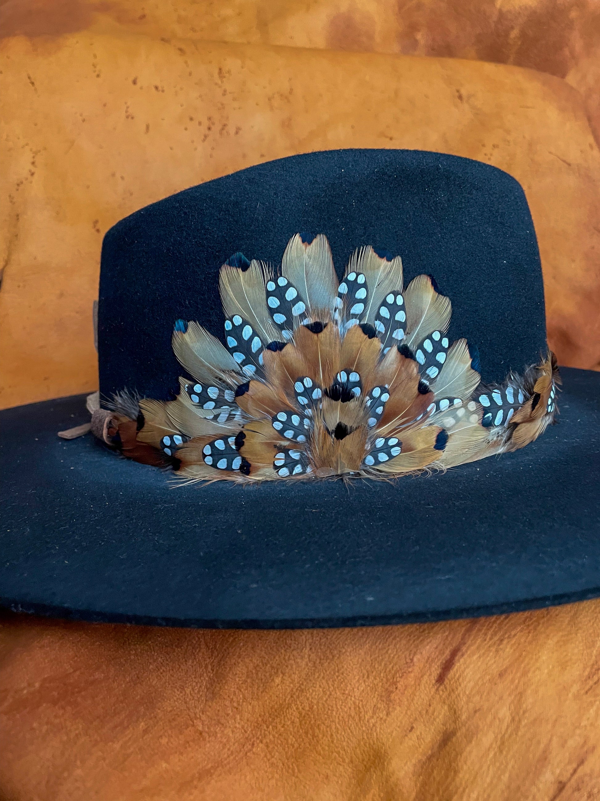Side view of a handmade feather hatband and medallion with golden pheasant and quail feathers with black polka dot accents,
styled on a black felt hat.