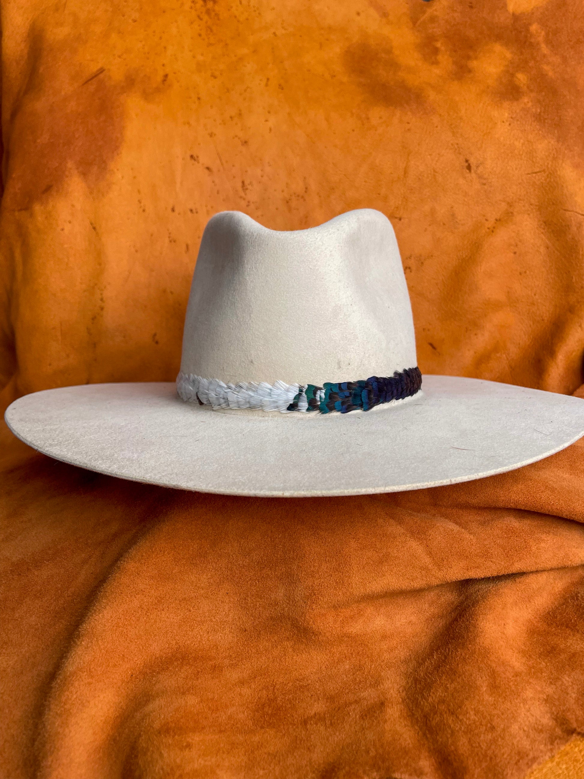 Handmade feather hatband with green, white, and rust pheasant feathers on a cream felt hat.