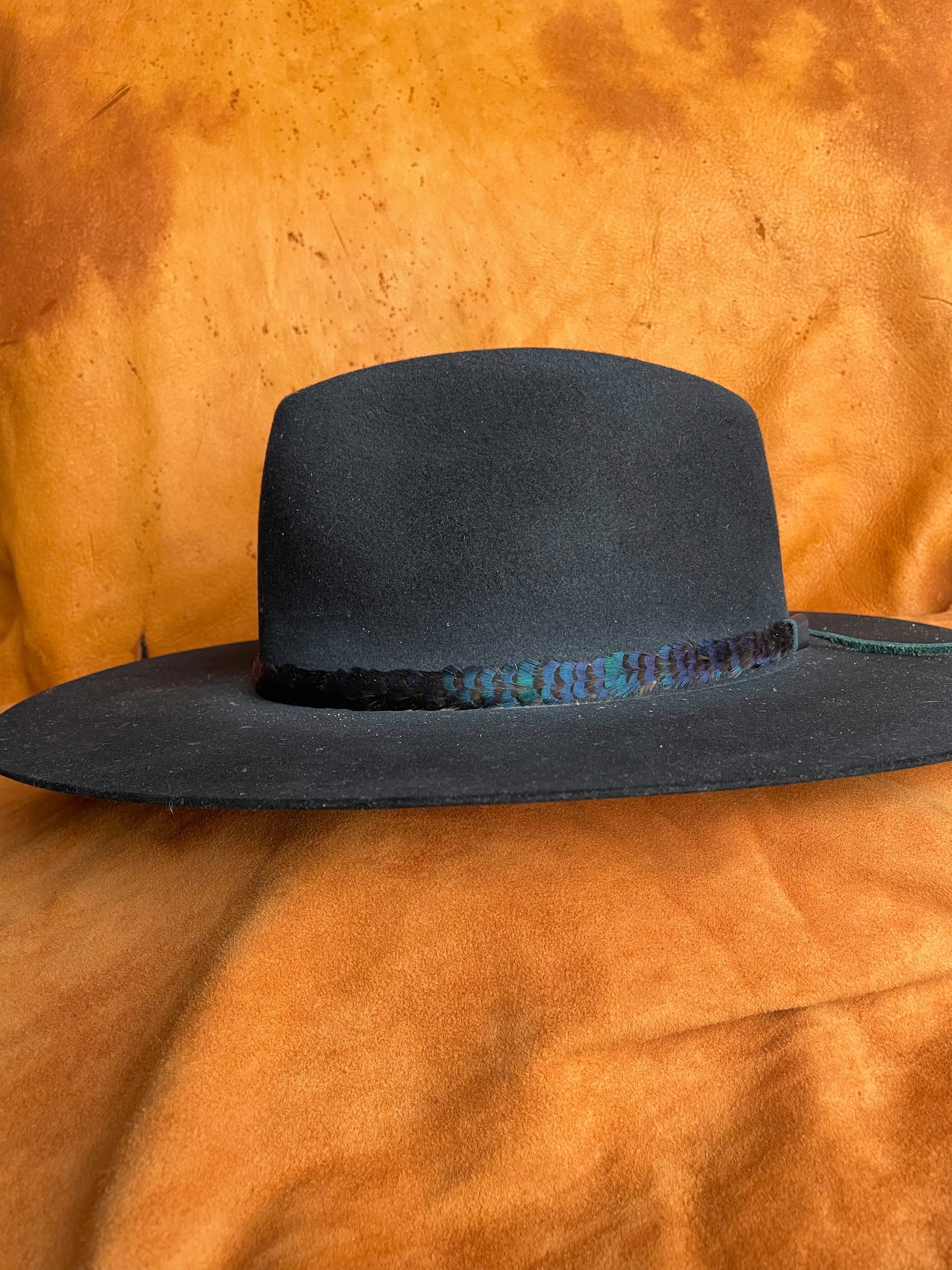 Handmade pheasant feather hatband with iridescent green and blue tones on a black felt hat. 