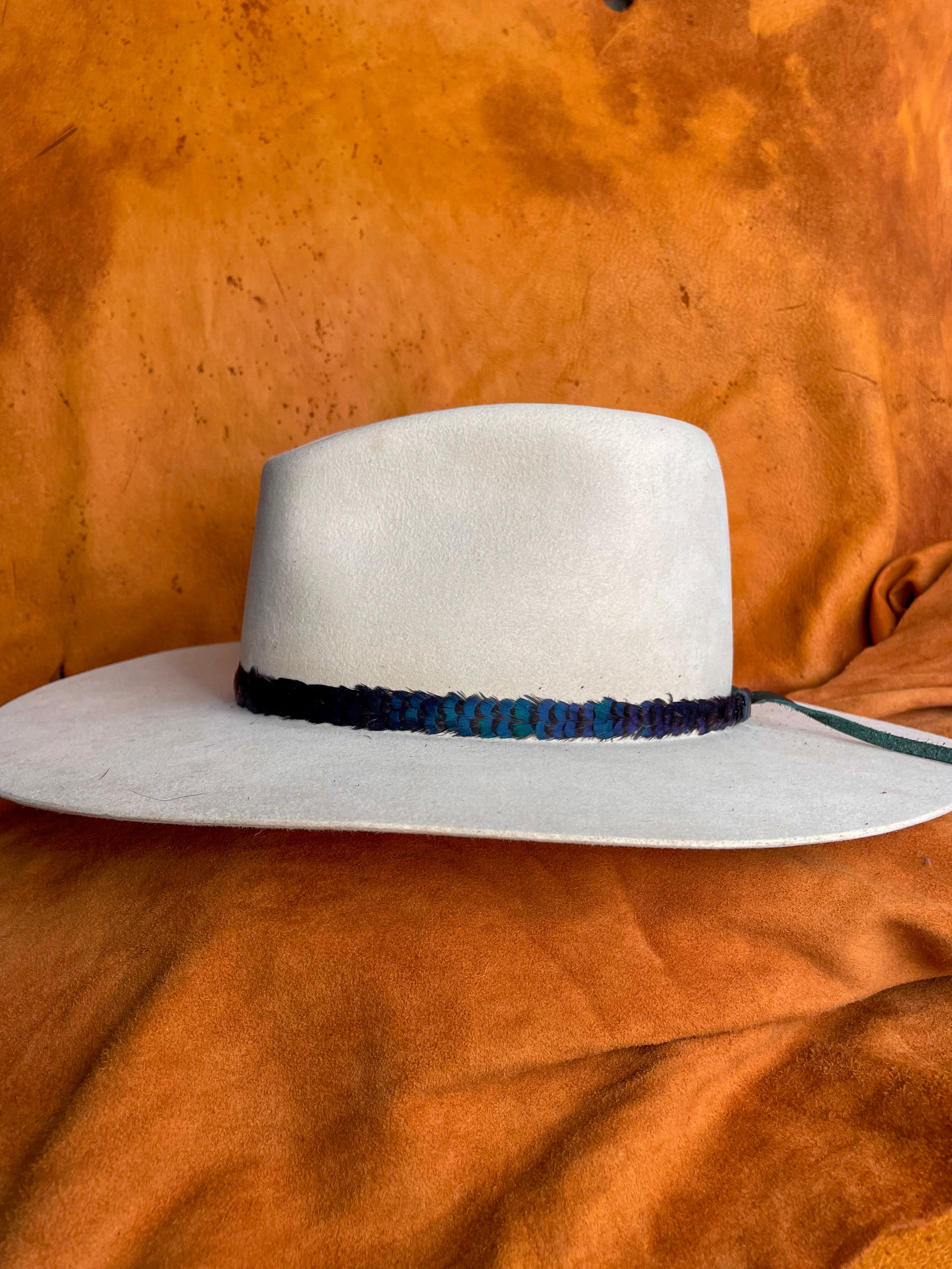 Side view of a minimalist feather band with jewel-toned color on an ivory felt hat.